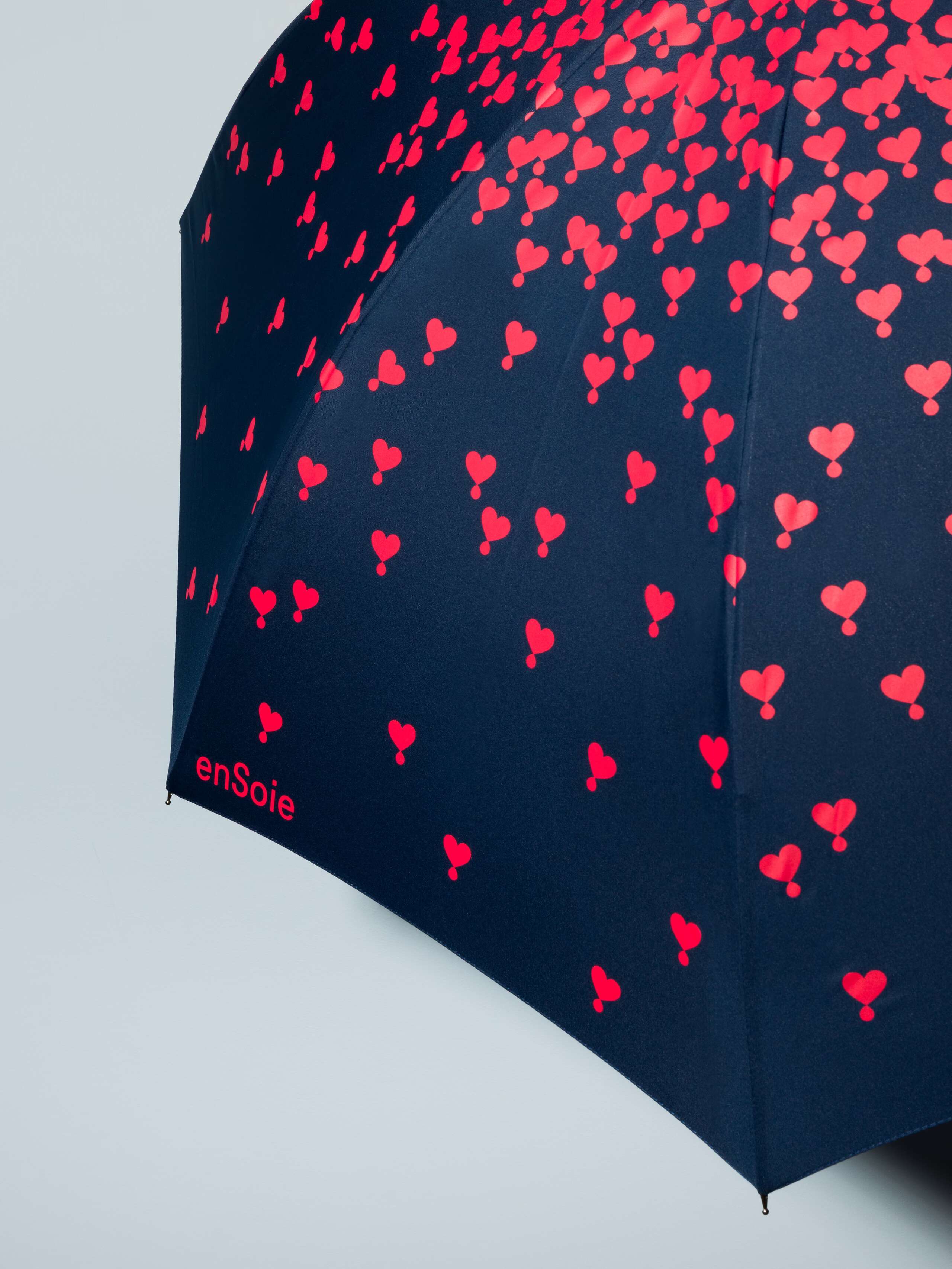 Picture of a detail of a navy blue umbrella featuring a red heart print