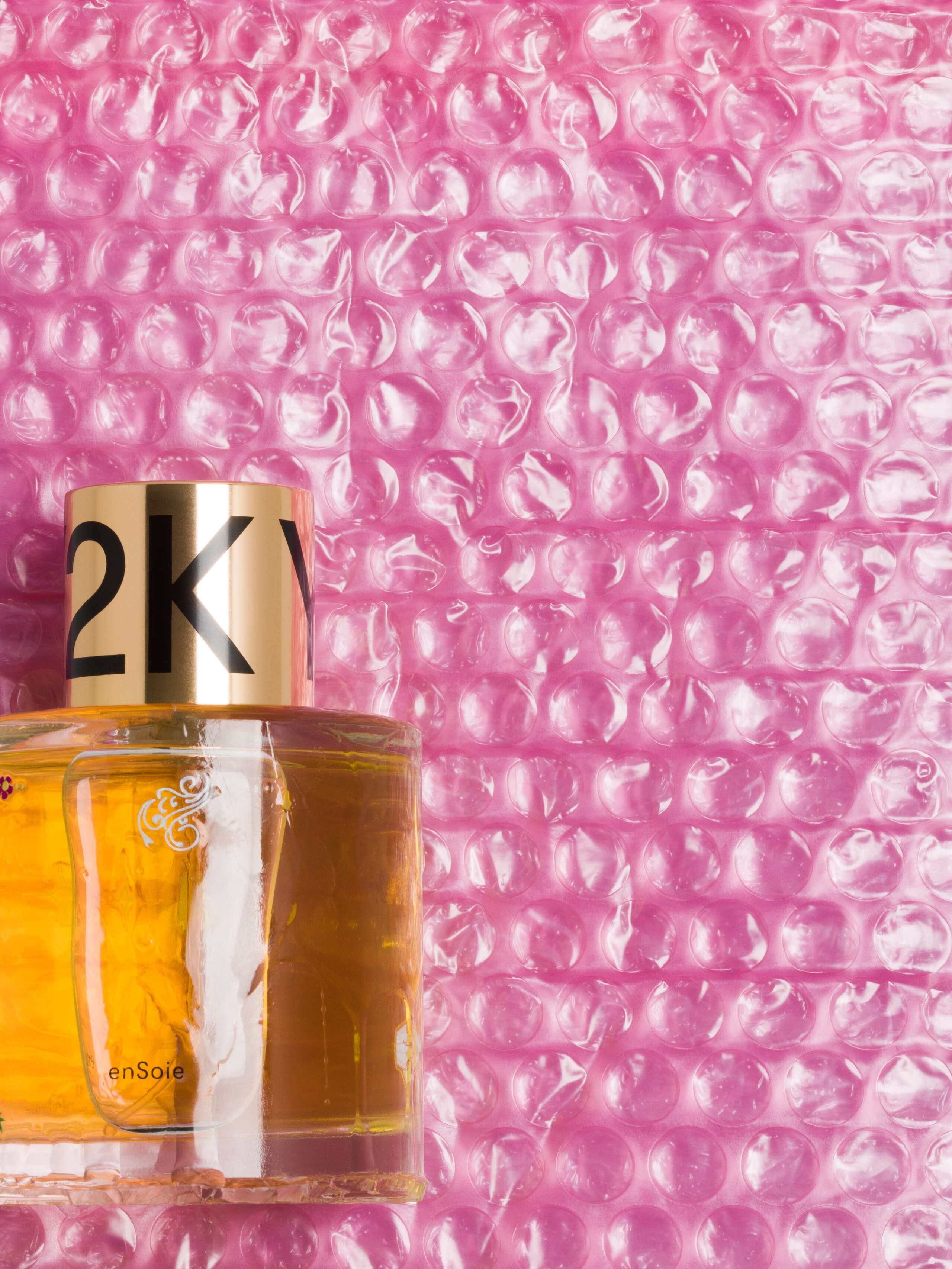 Picture of a artfully designed perfume flacon with the name Y2K in front of a pink bubble wrap. The design is made by French artist Caroline Ventura.