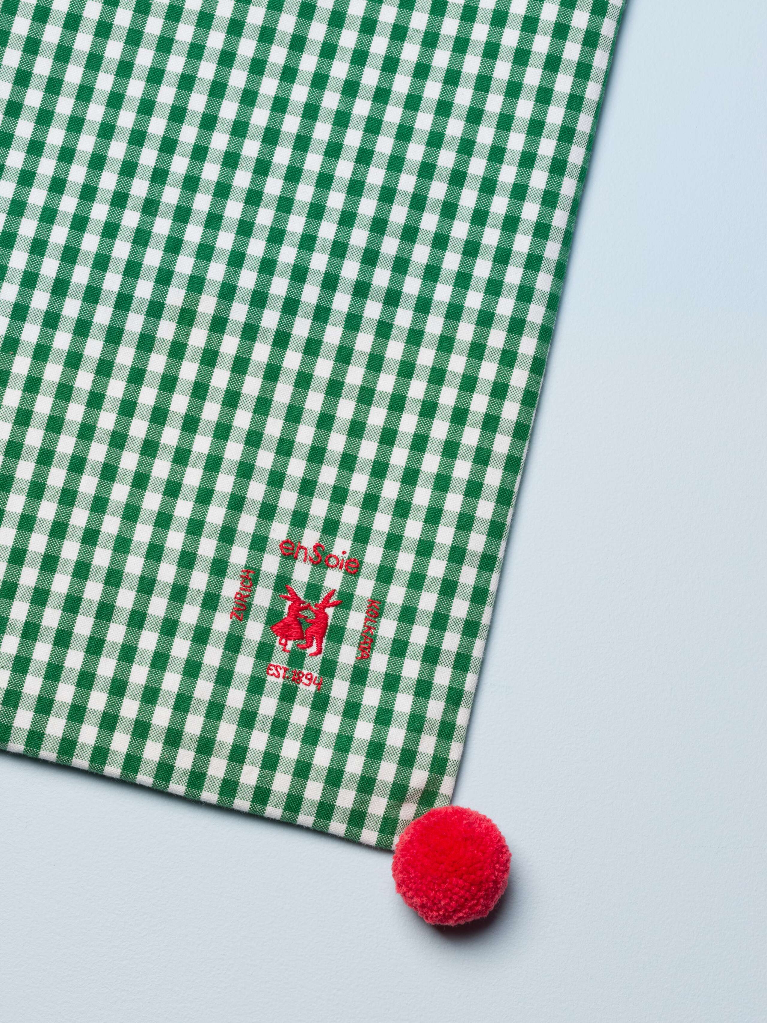 Picture of a detail of a green cotton tote bag featuring a red pompom