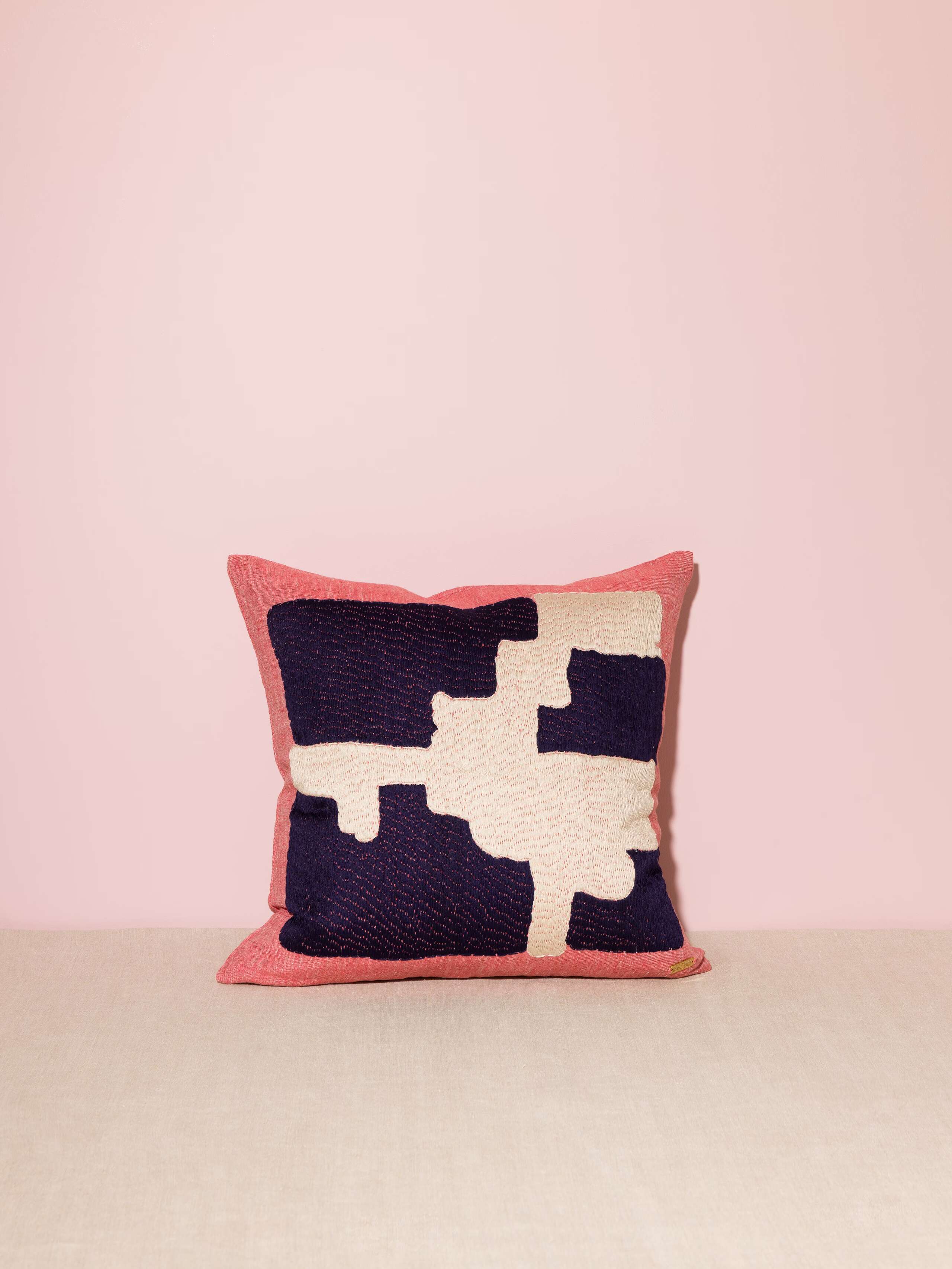 Picture of a red linen pillow featuring a navy blue and off-white embroidery