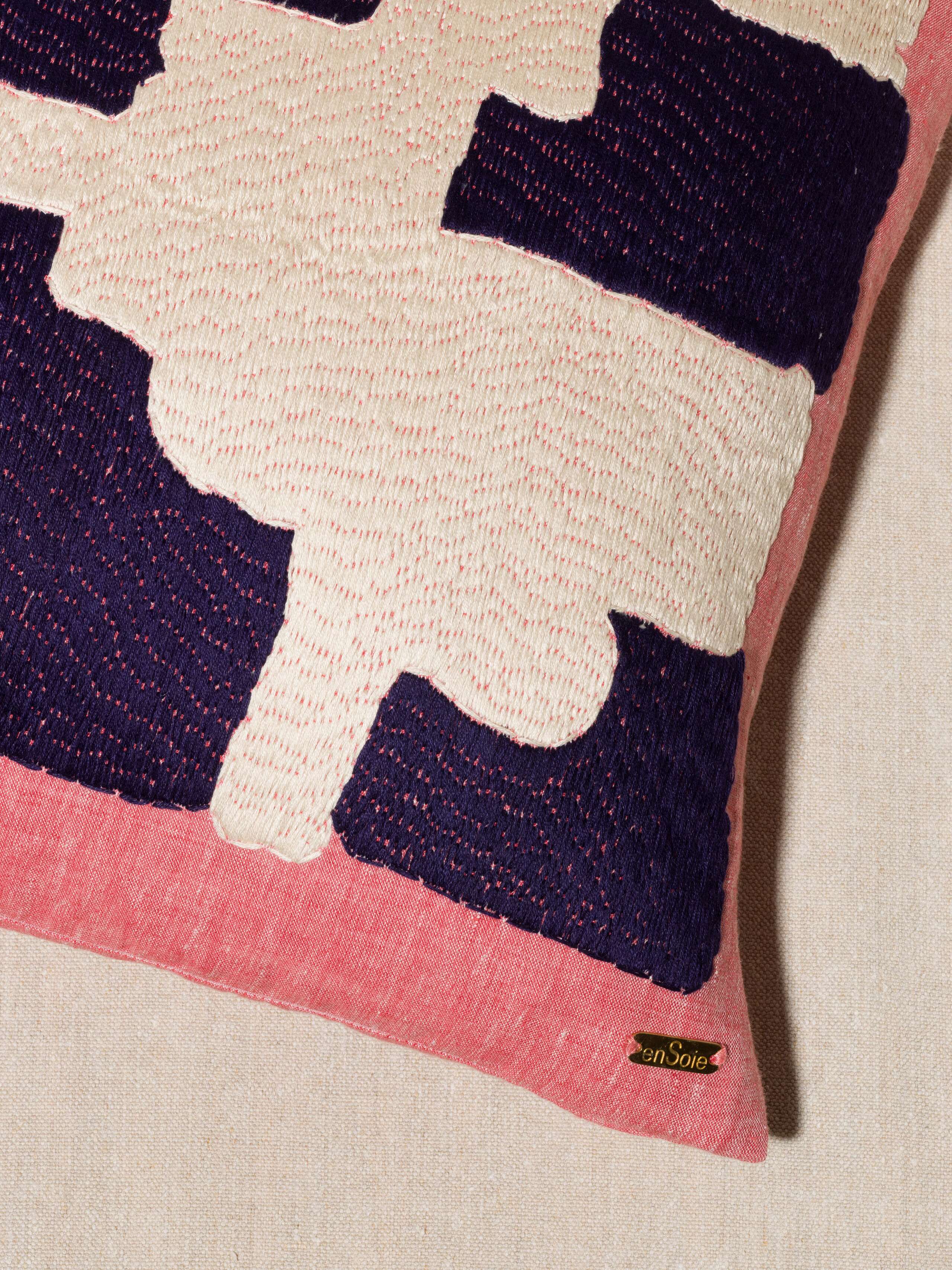 Picture of a red linen pillow featuring a navy blue and off-white embroidery