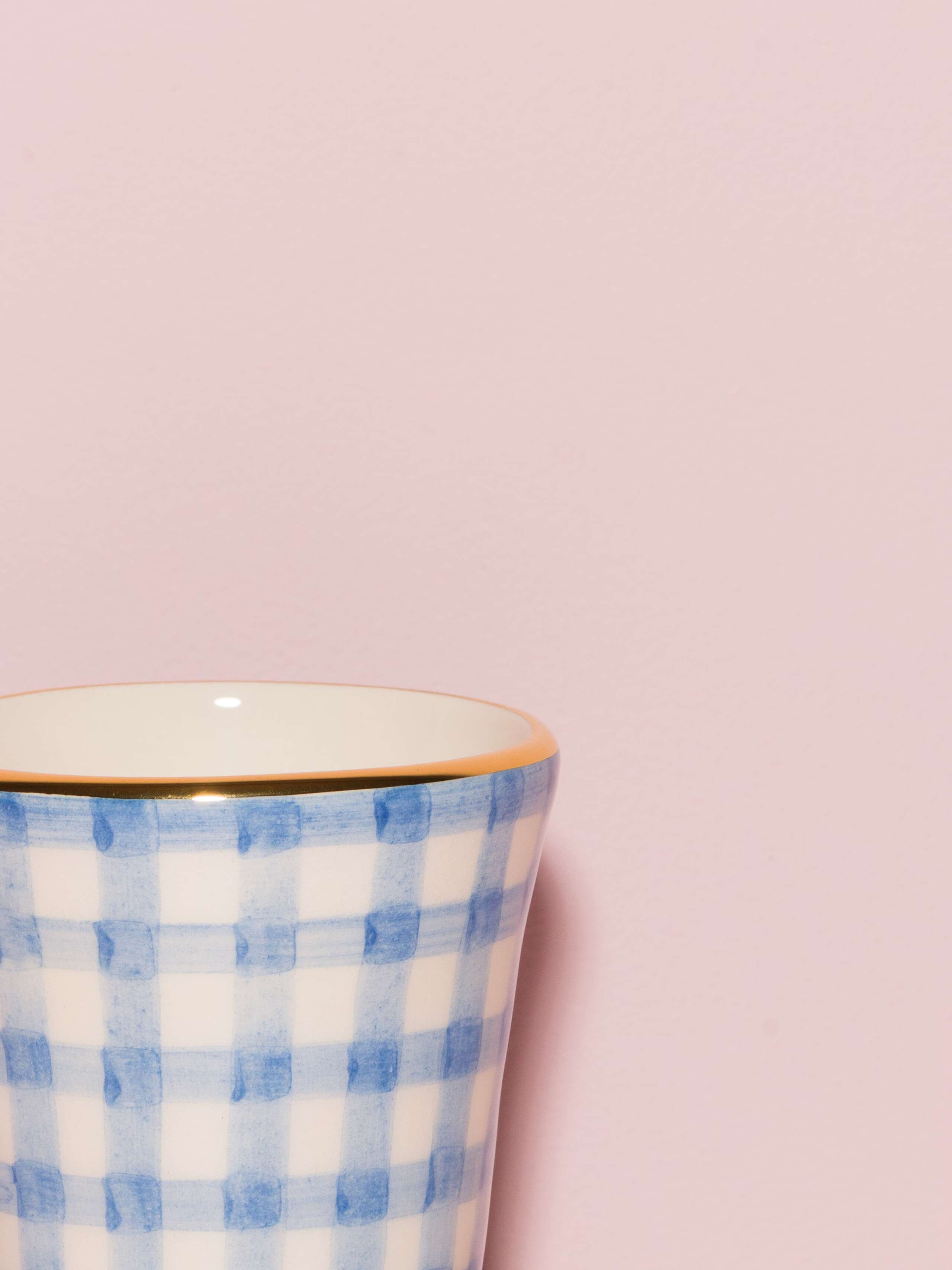 Picture of a detail of an espresso cup featuring a golden rim and a light blue vichy check pattern