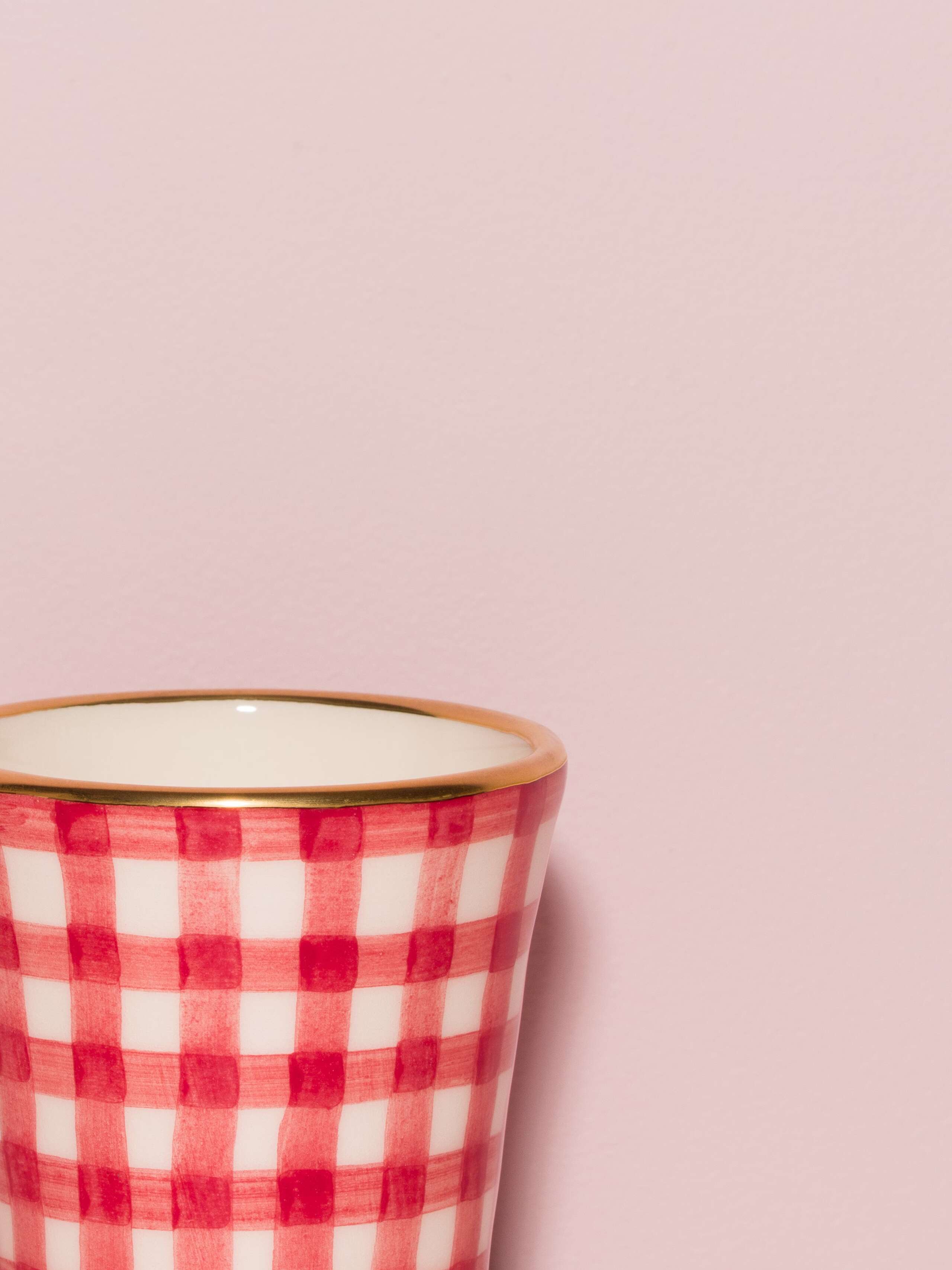 Picture of a detail of an espresso cup featuring a golden rim and a red vichy check pattern