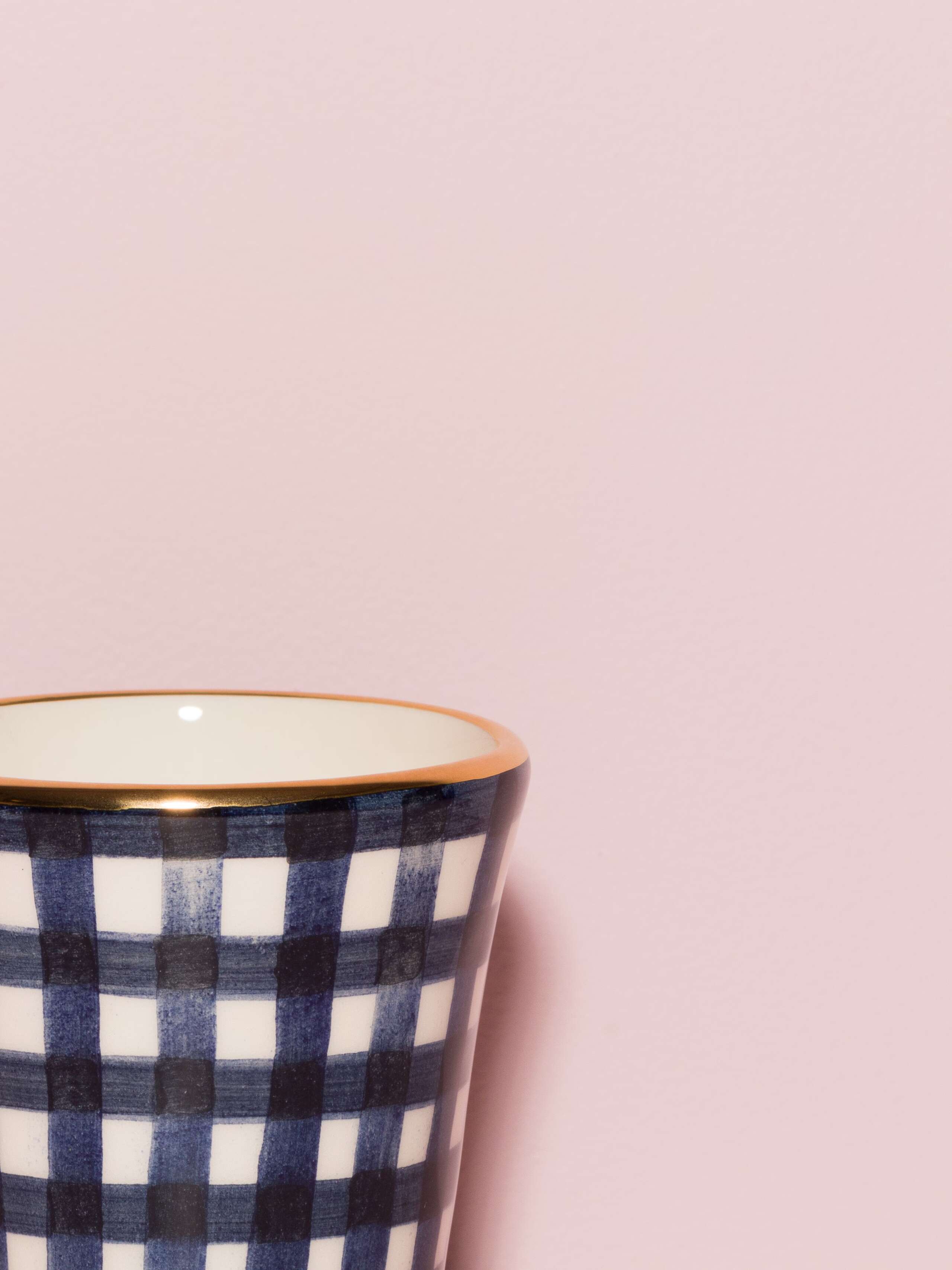 Picture of a detail of an espresso cup featuring a golden rim and a navy blue vichy check pattern