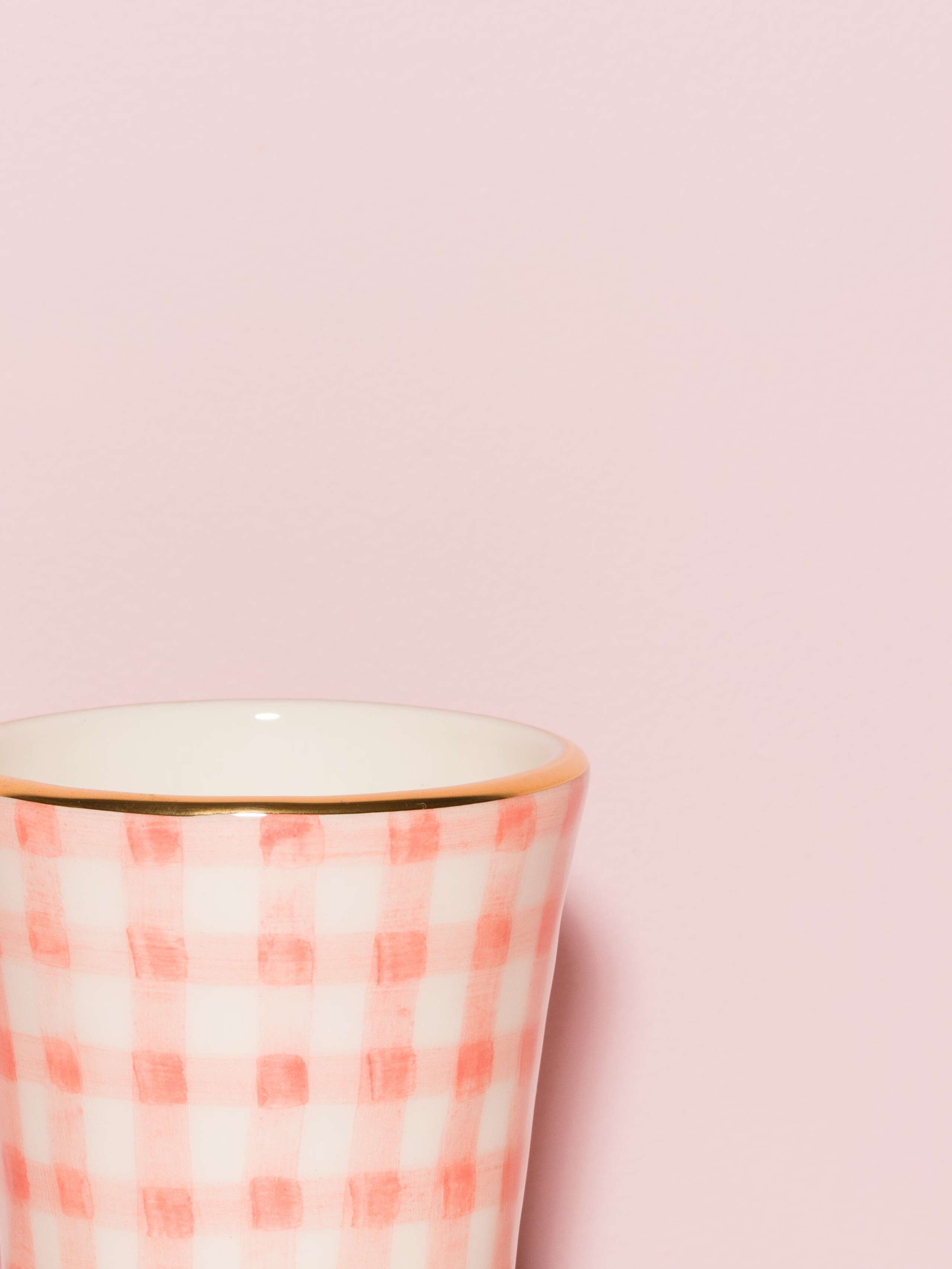 Picture of a detail of an espresso cup featuring a golden rim and a pink vichy check pattern