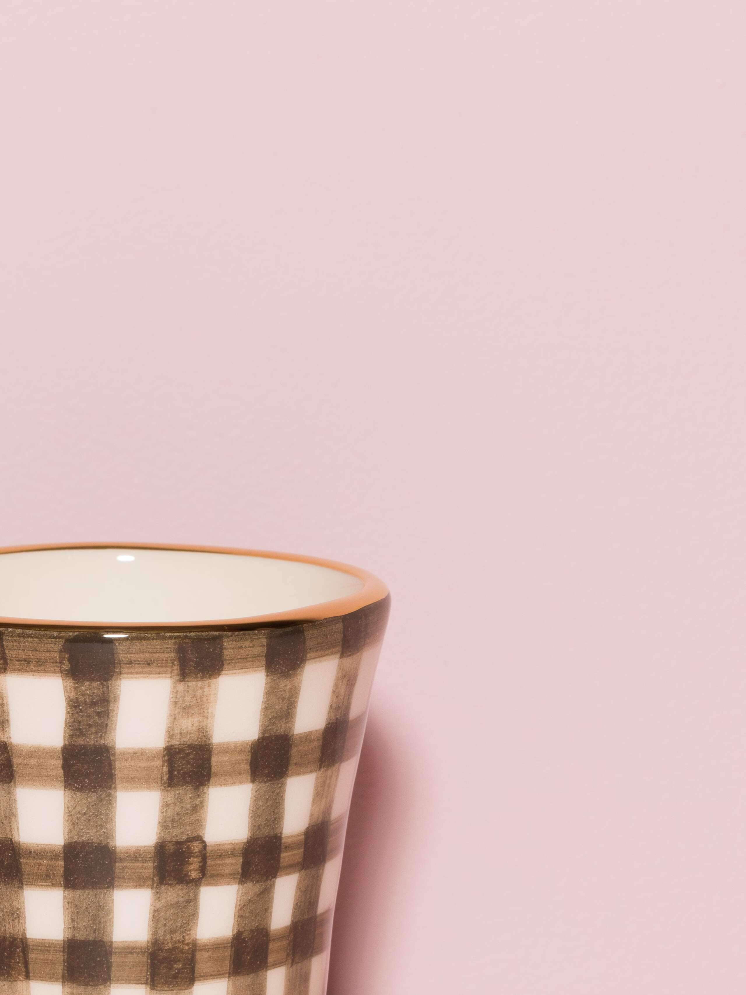 Picture of a detail of an espresso cup featuring a golden rim and a beige check pattern