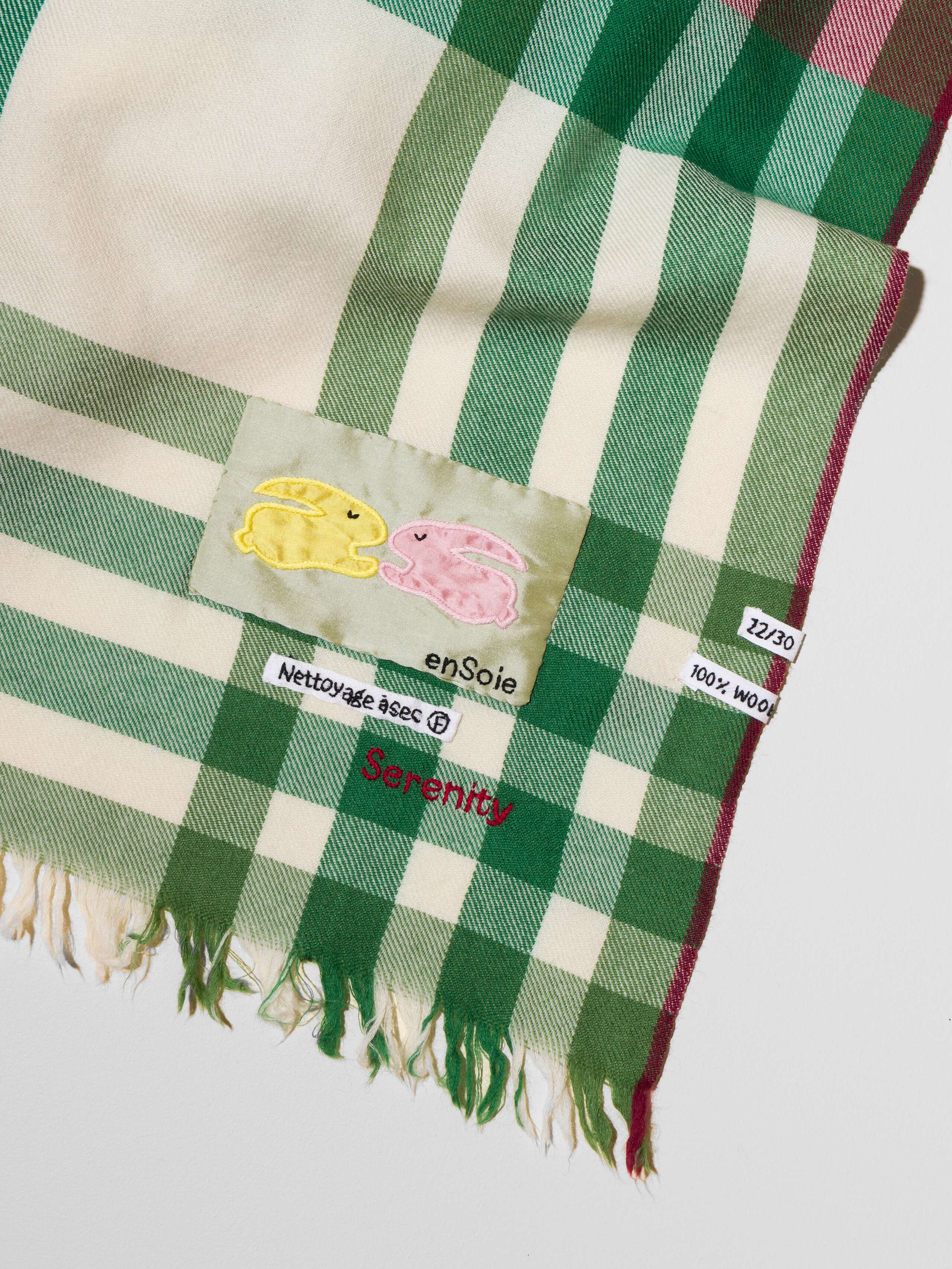 Picture of a detail of a wool scarf in a light beige shade featuring a green and red check pattern
