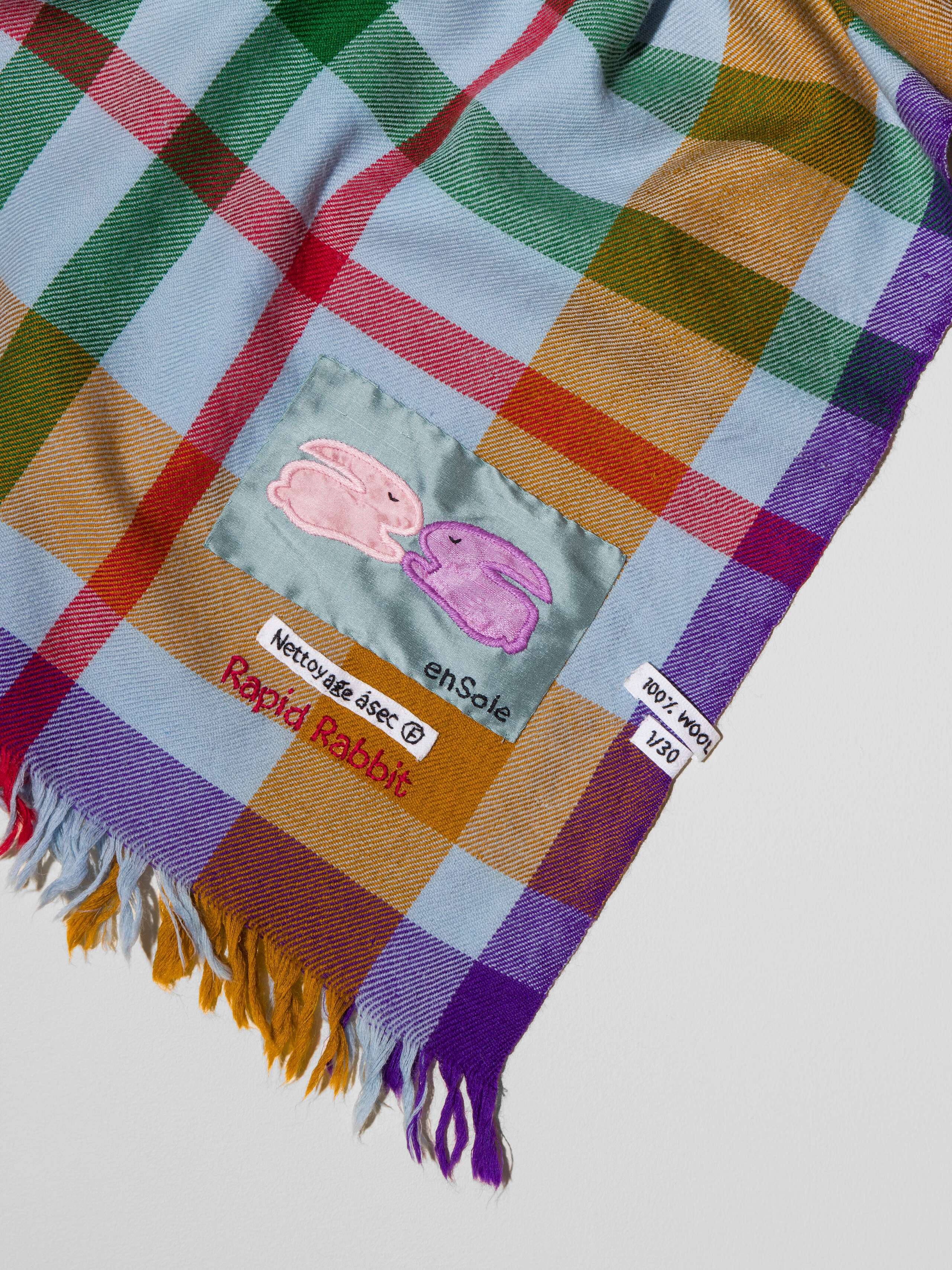 Picture of a wool scarf in a beautiful blue grey shade featuring a check pattern in green, purple, brown and red shades