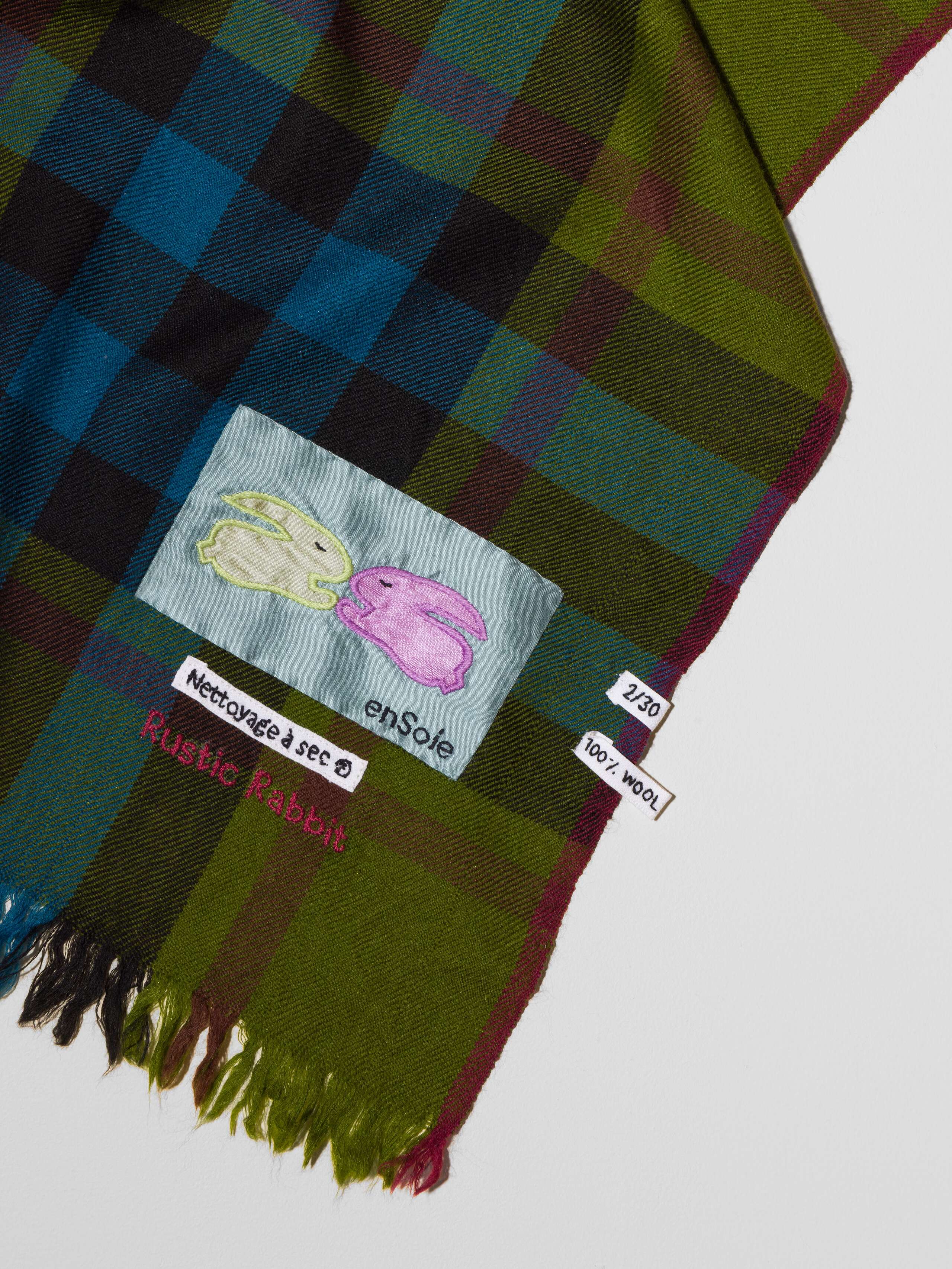 Picture of a wool scarf in a beautiful olive green shade featuring a check pattern in petrol blue and bordeaux red shades
