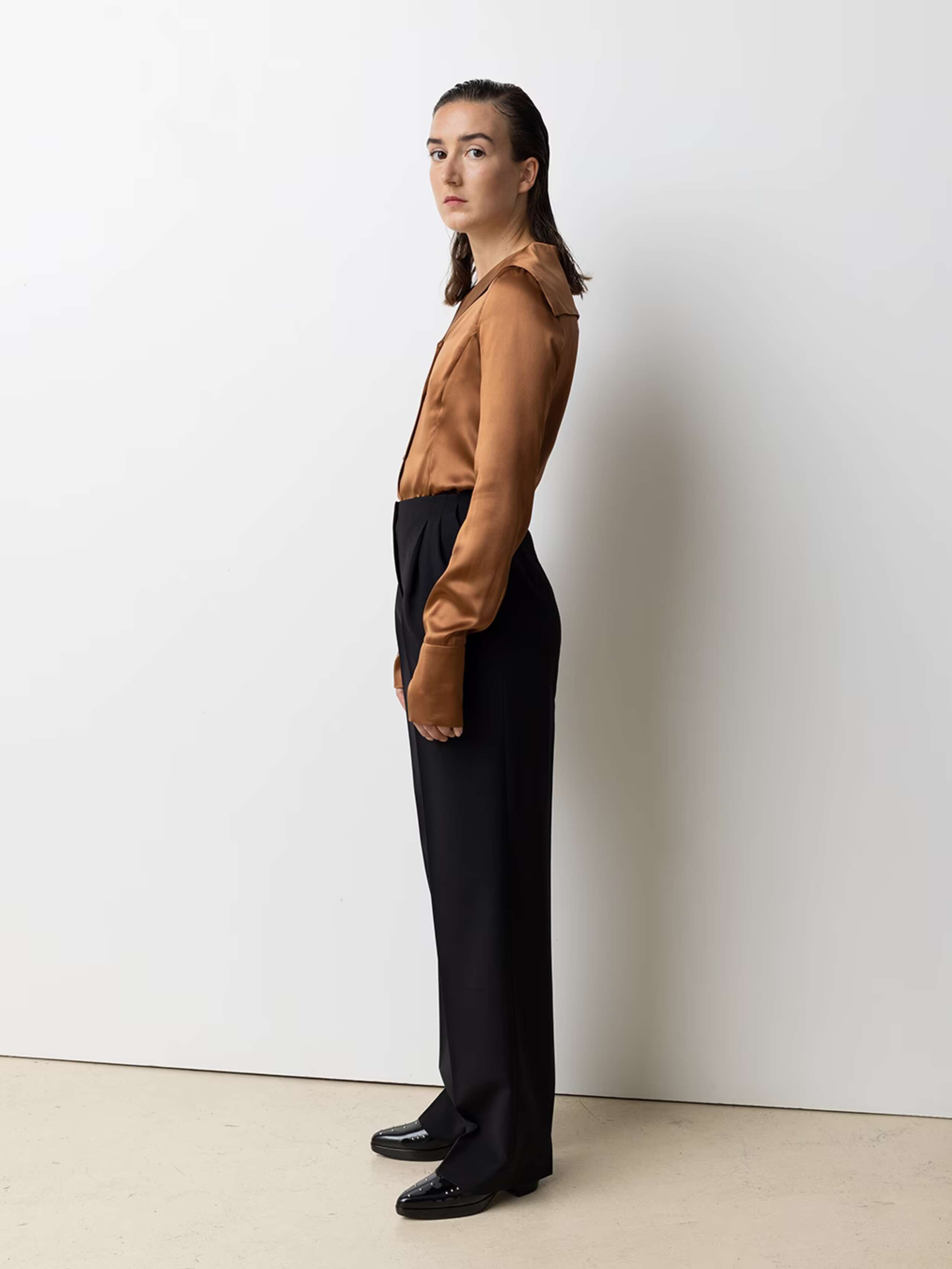 Picture of a female model wearing a brown silk blouse in combination with black wool trousers
