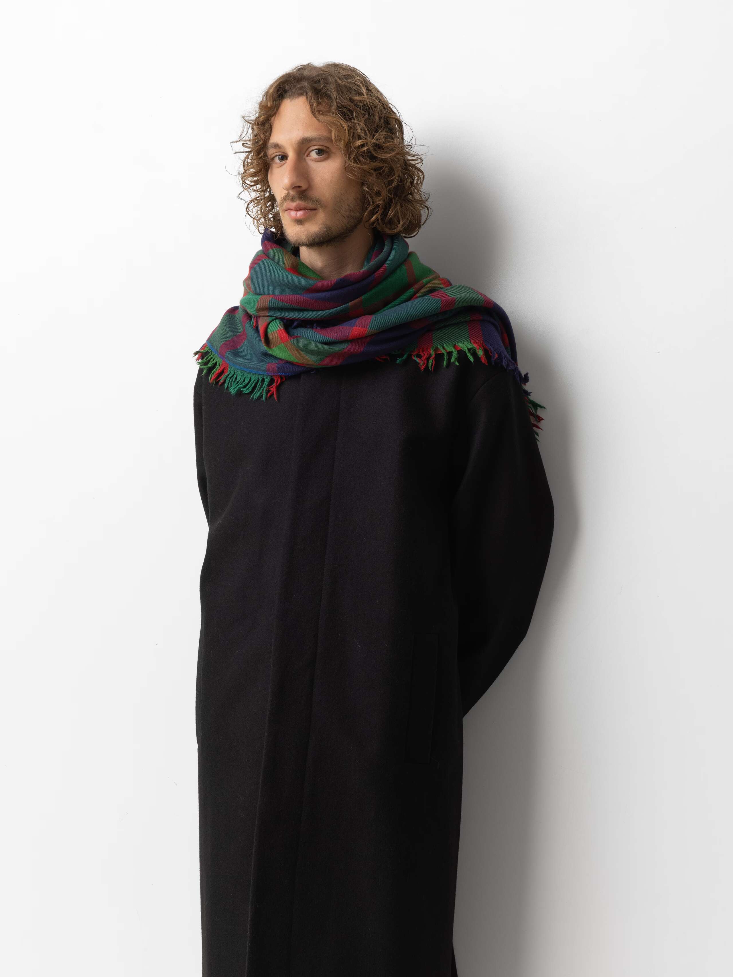 Picture of a male model wearing a black winter coat combined with a wool scarf in dark green, red and navy blue shades