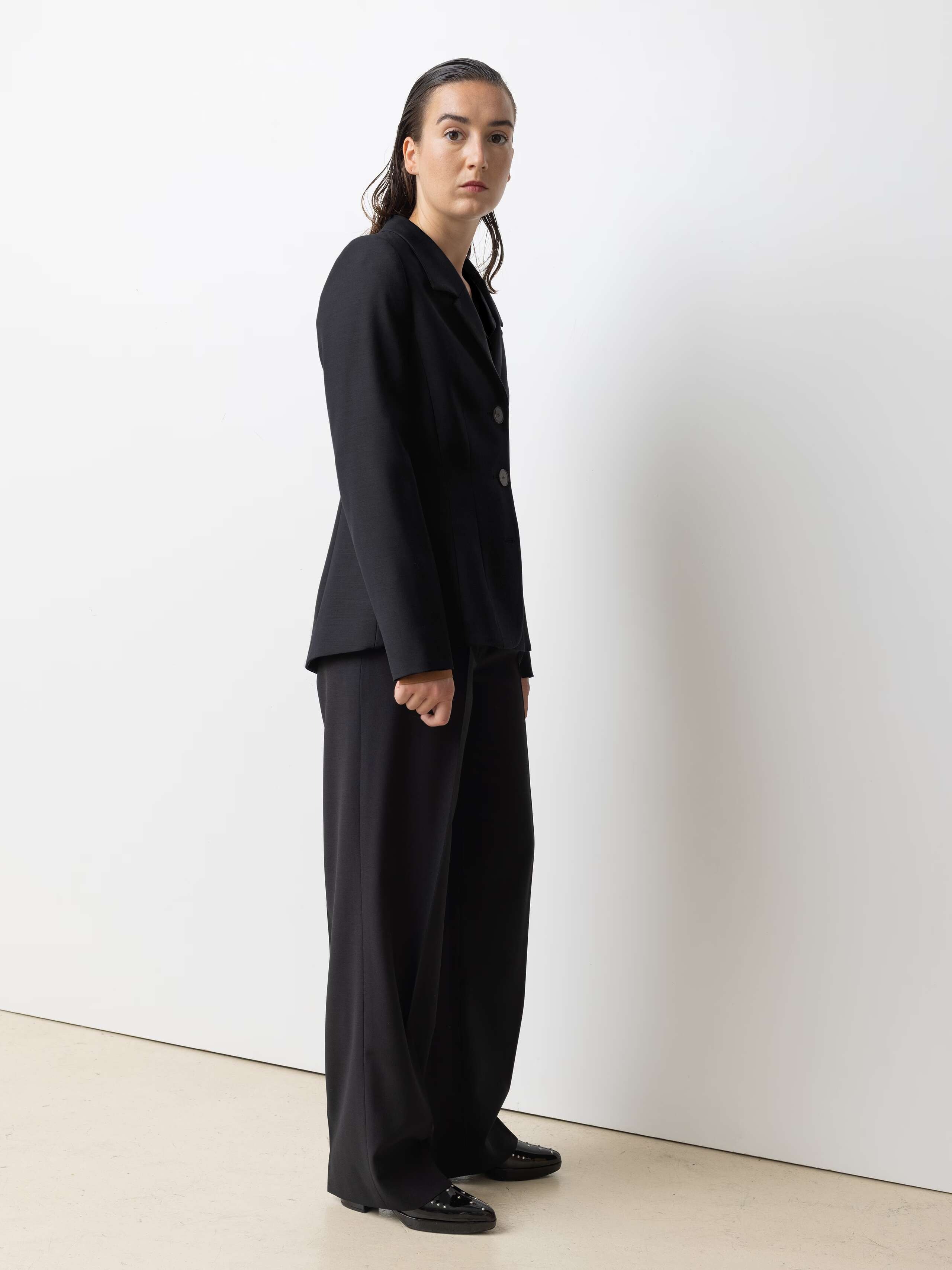 Picture of a female model wearing a black cool wool blazer in combination with matching pants and a brown shiny silk blouse 