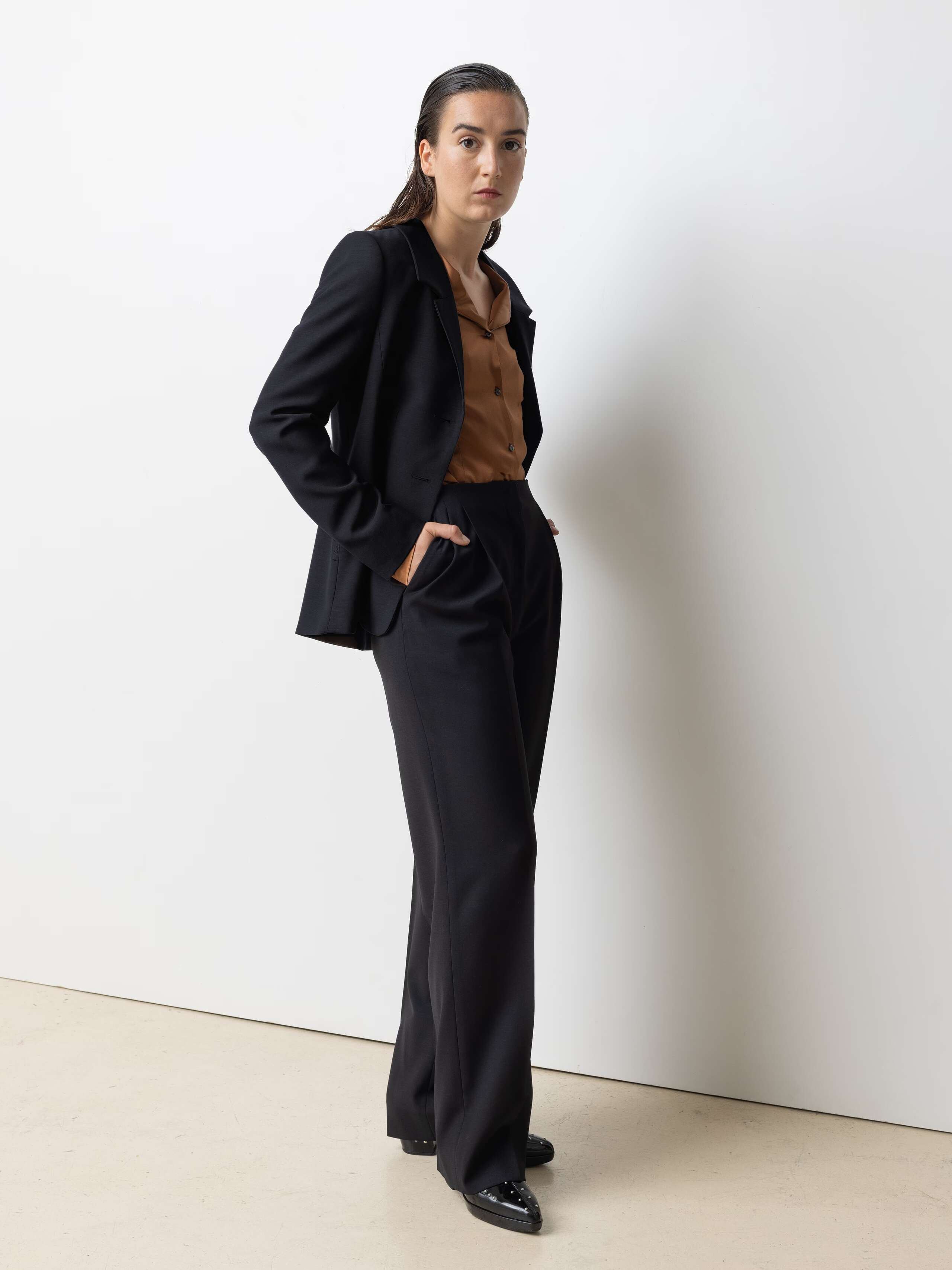 Picture of a female model wearing a black cool wool blazer in combination with matching pants and a brown shiny silk blouse 
