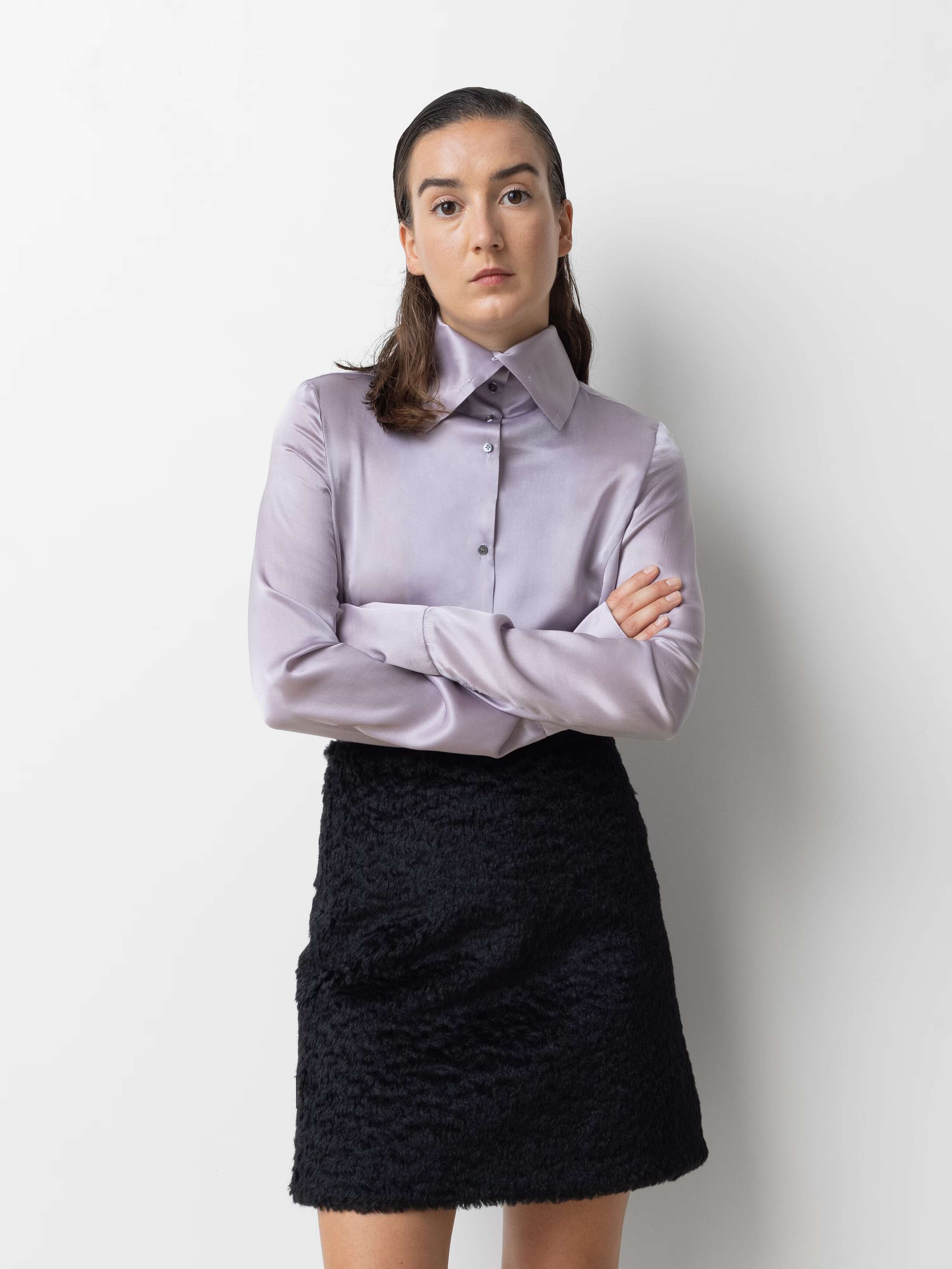 Picture of a female model wearing a short black skirt in combination with a silk blouse in a delicate lavender shade