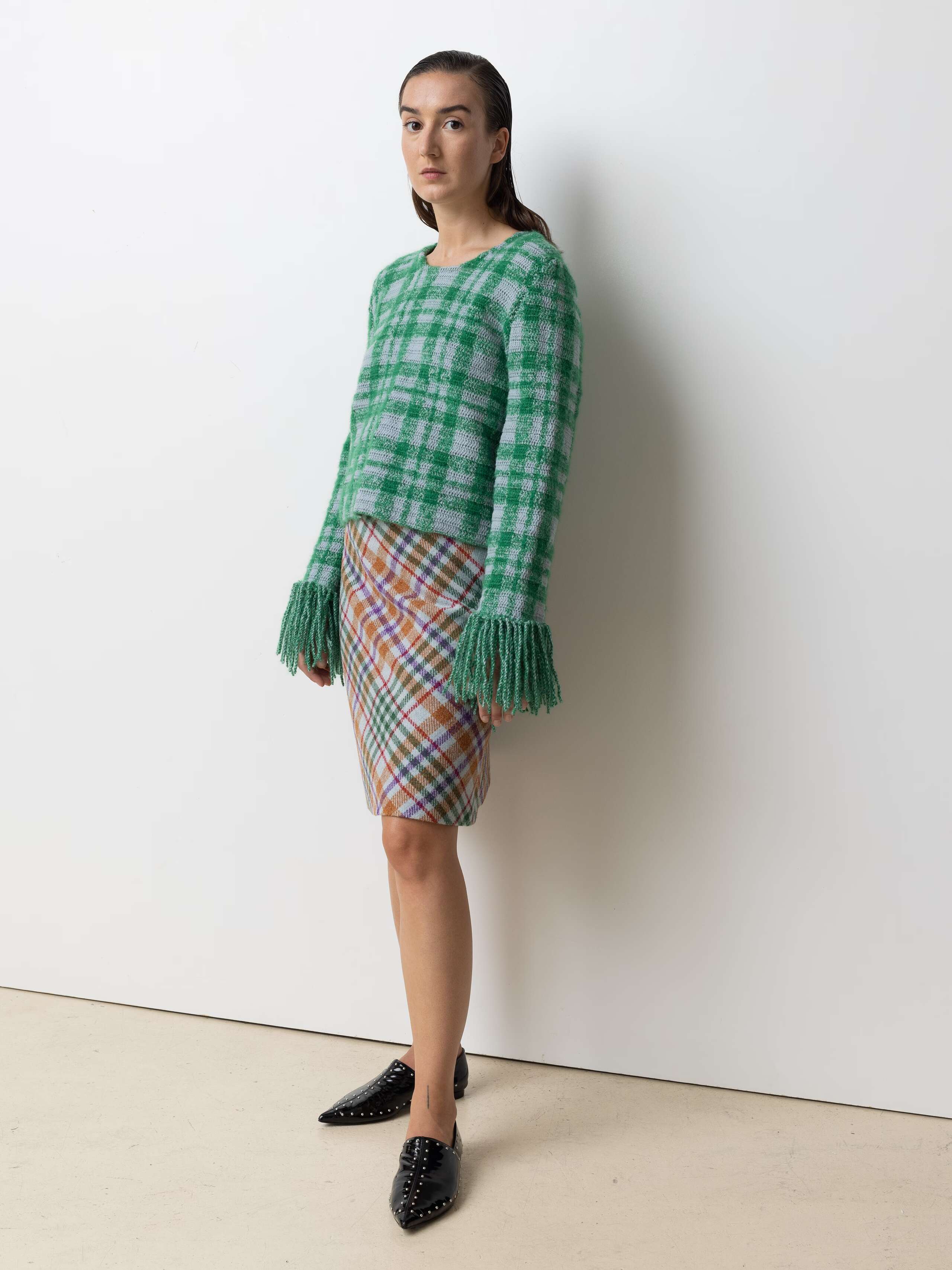 Picture of a femle model wearing a colourful wool skirt in combination with a green wool pullover
