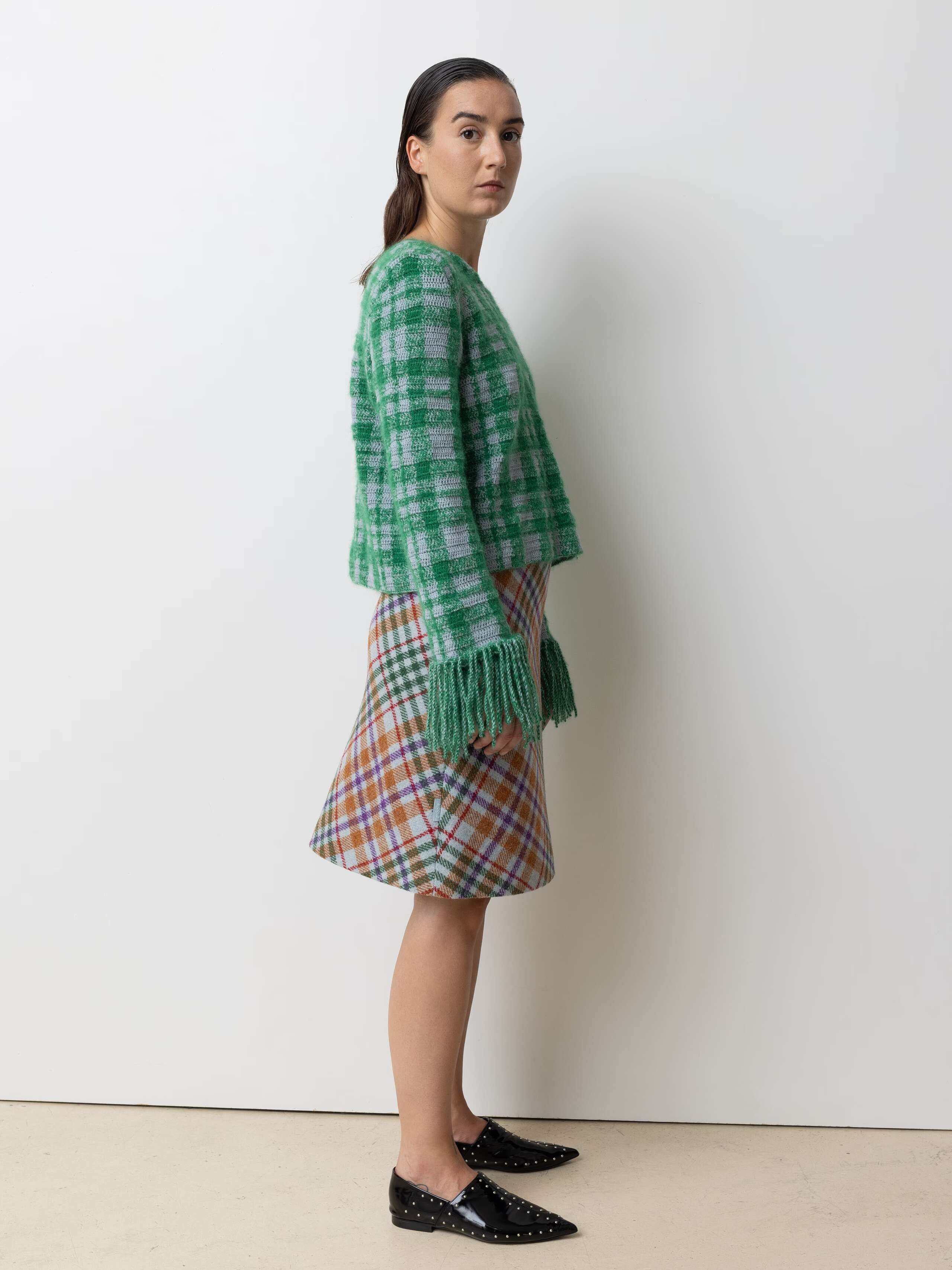 Picture of a femle model wearing a colourful wool skirt in combination with a green wool pullover