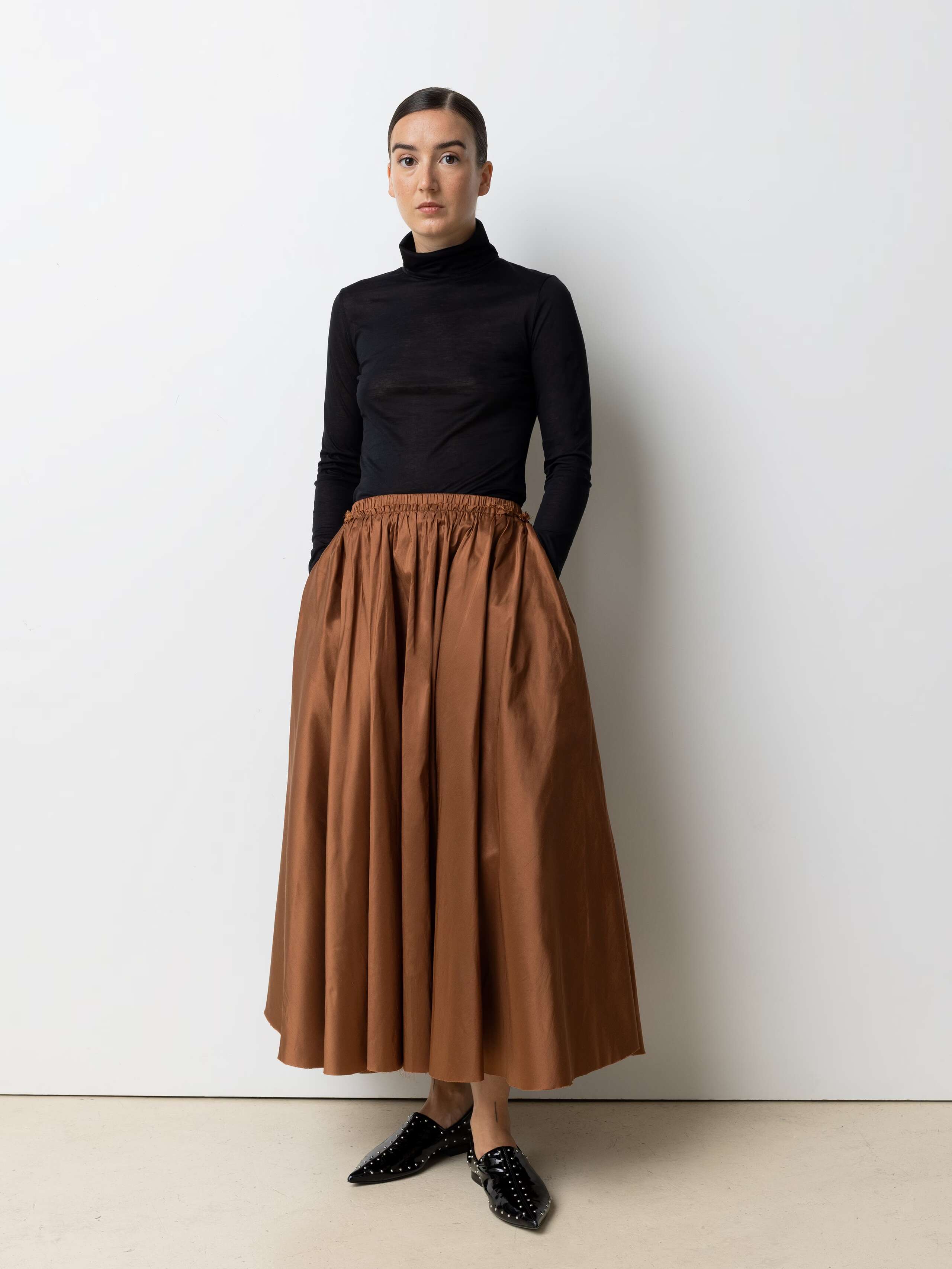 Picture of a female model wearing a combination of a classic black turtleneck and a brown silk skirt