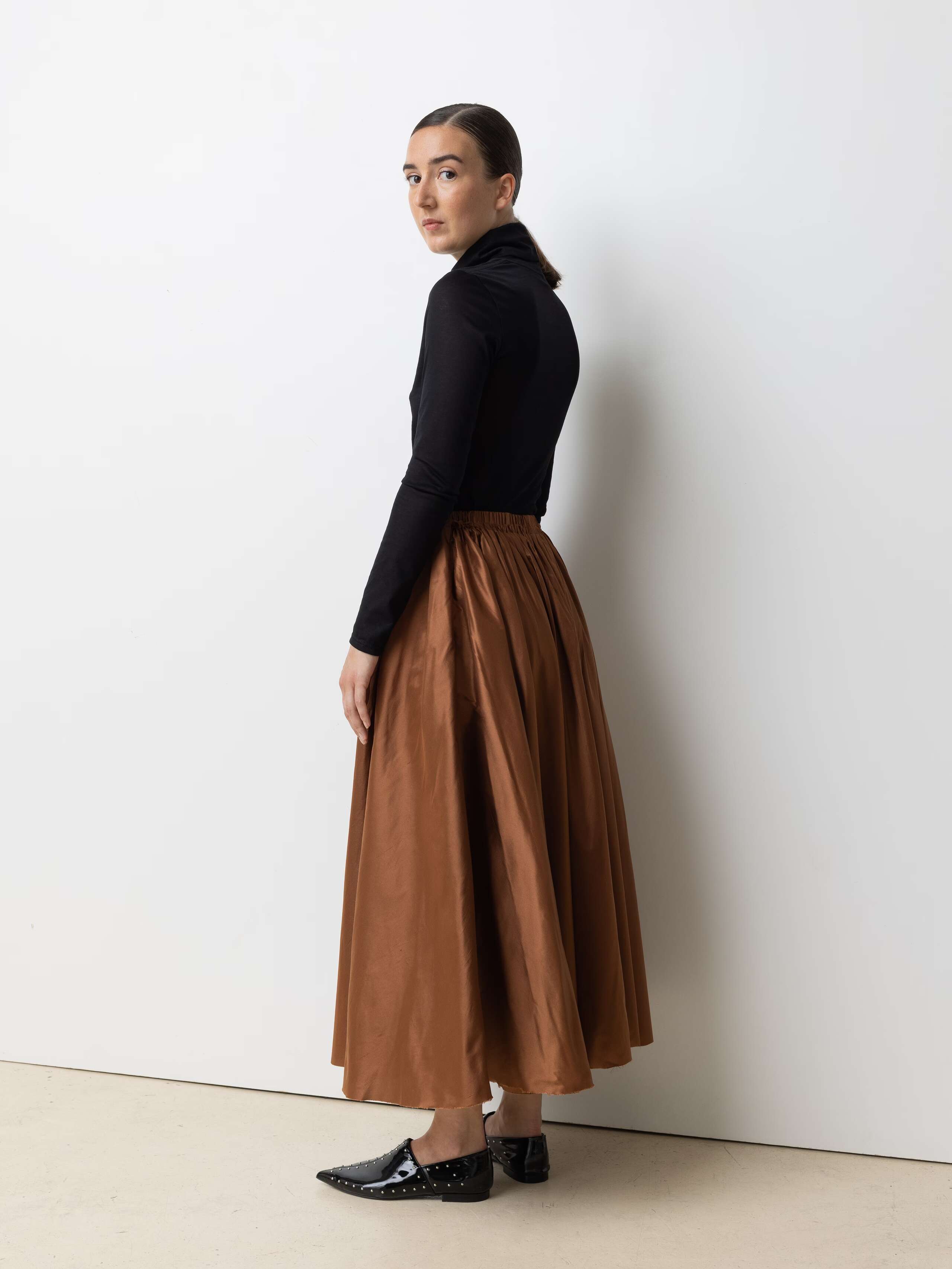 Picture of a female model wearing a combination of a classic black turtleneck and a brown silk skirt