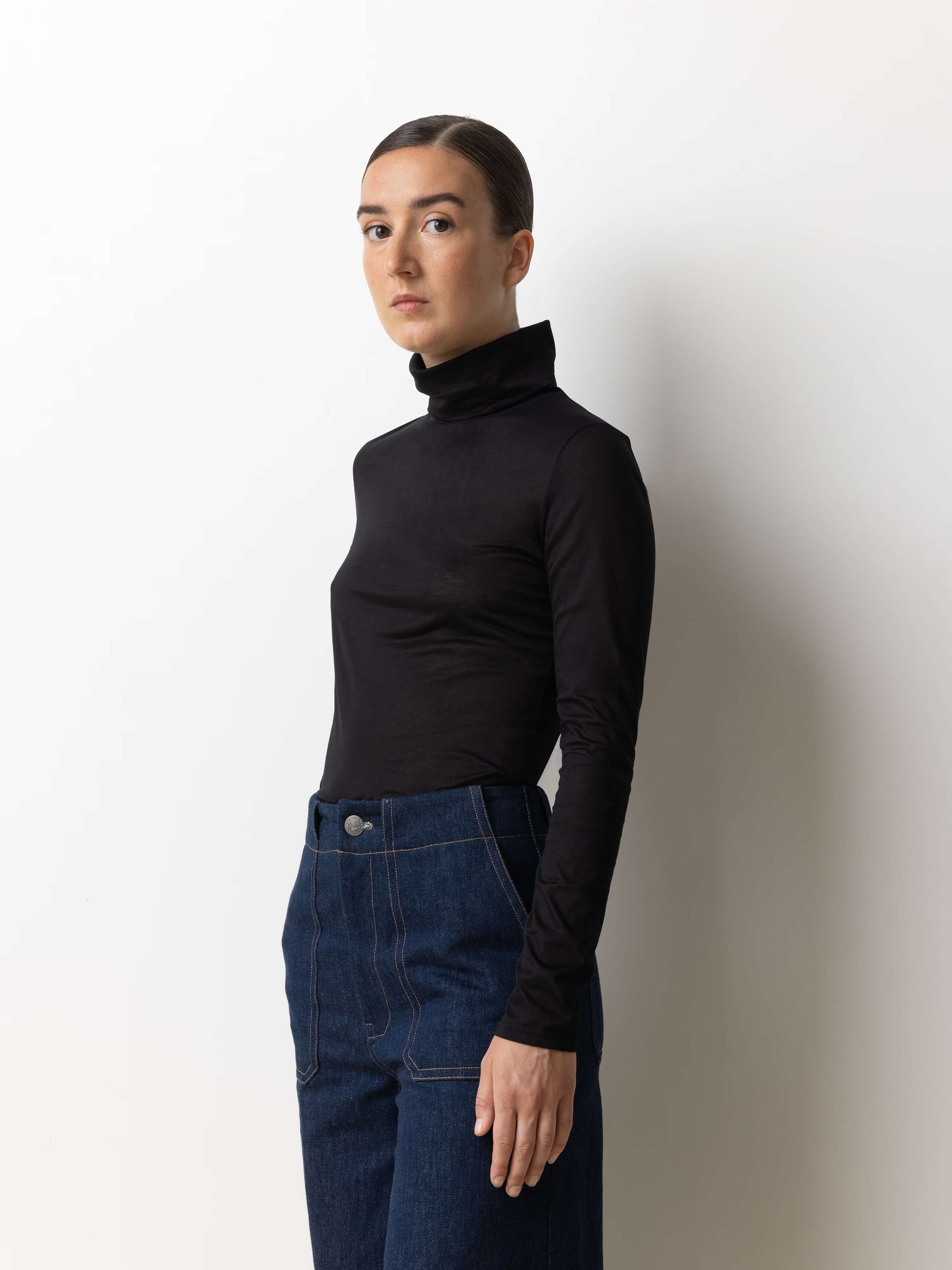 Female model wearing a tight fitting turtleneck jumper made of soft black cotton jersey