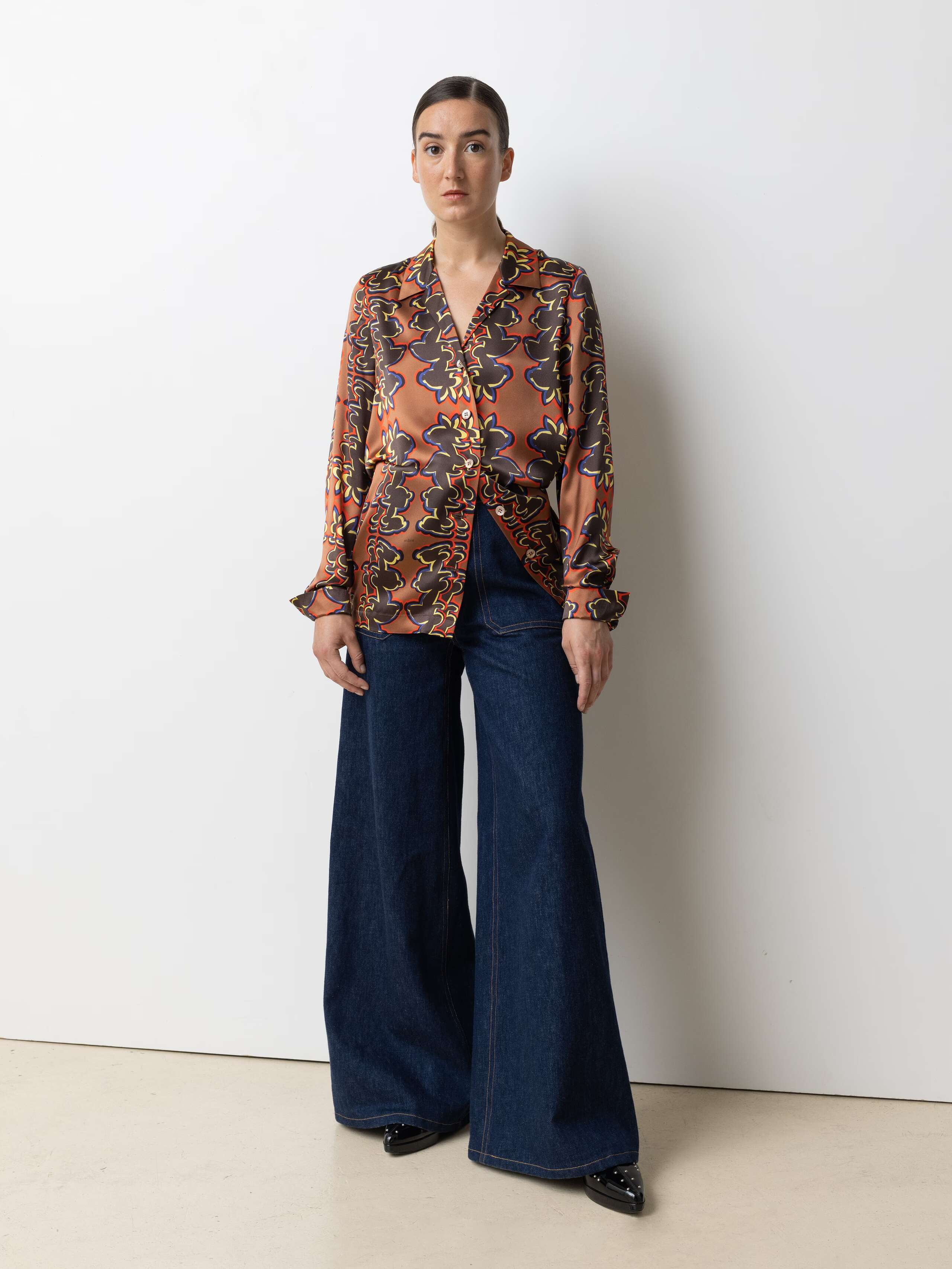 Picture of a model wearing a silk blouse in warm shades of brown, red and yellow in combination with a classic bleu jeans
