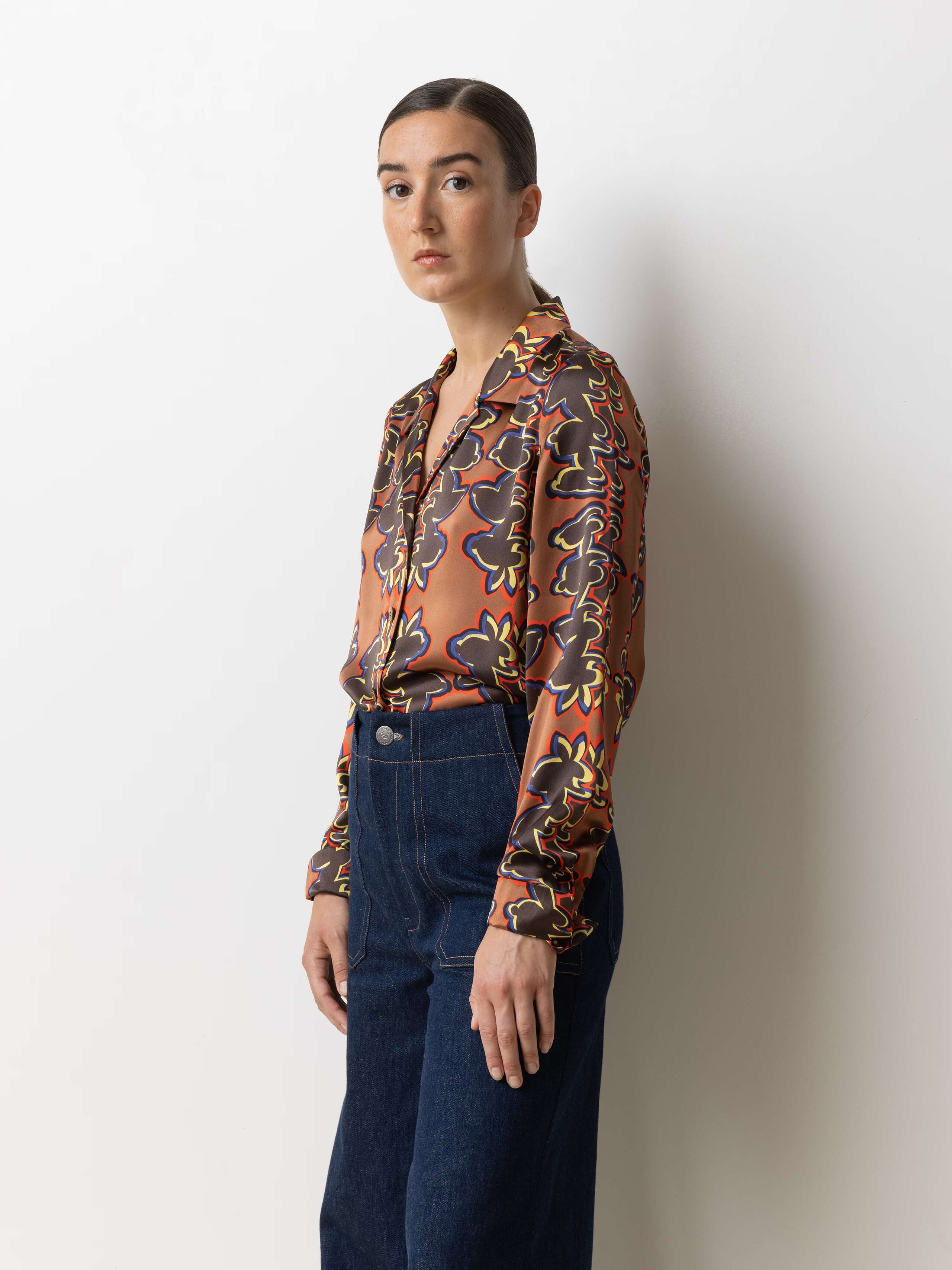 Picture of a model wearing a silk blouse in warm shades of brown, red and yellow in combination with a classic bleu jeans