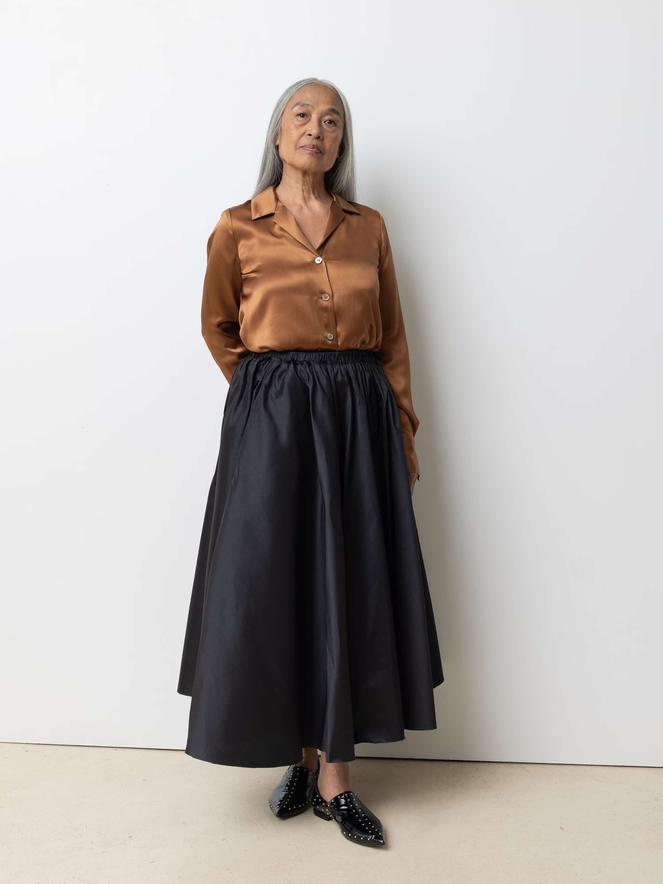 Picture of a female model wearing a combination of a shiny brown silk blouse and an black, airy silk skirt 