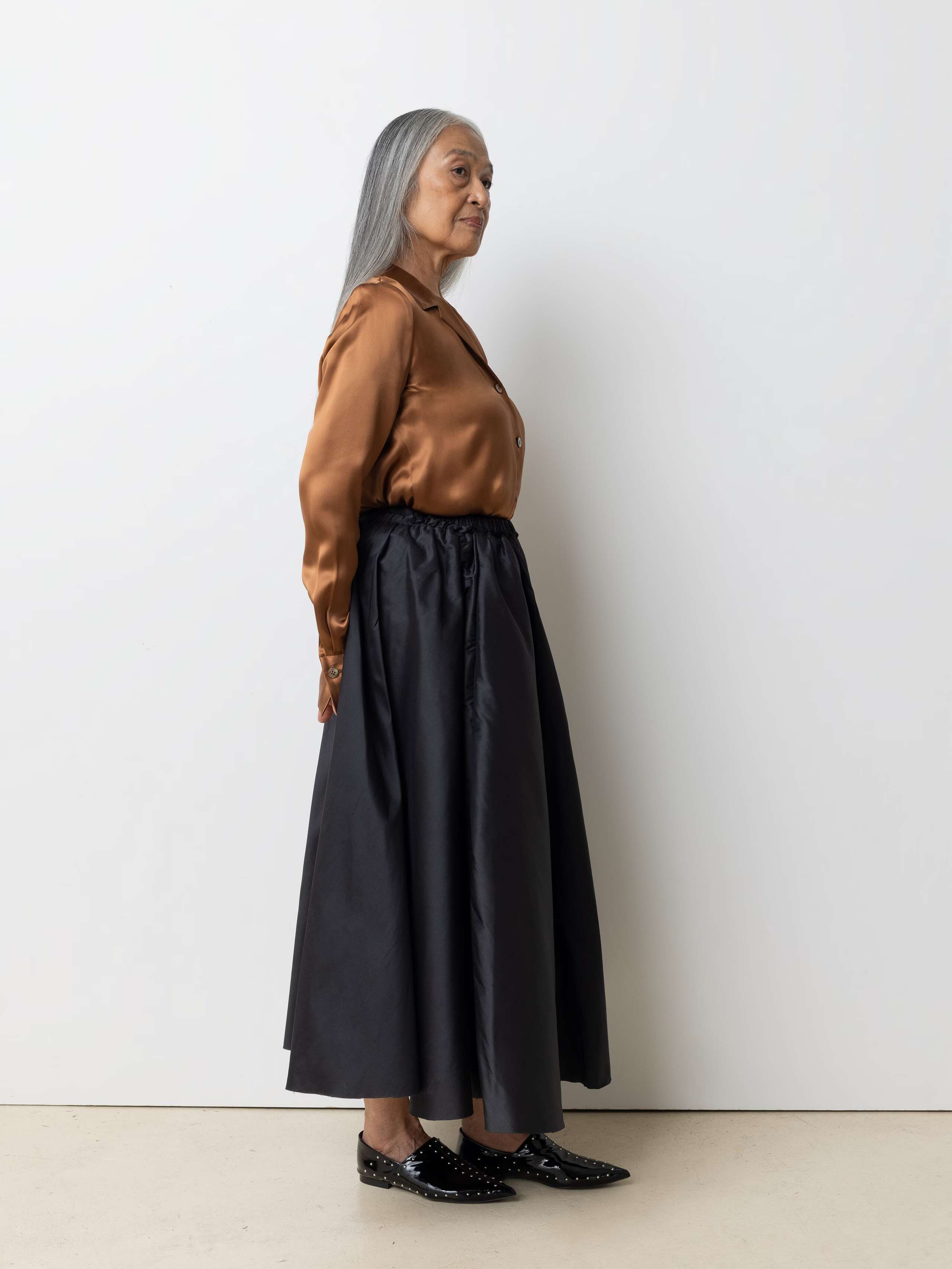 Picture of a female model wearing a combination of a shiny brown silk blouse and an black, airy silk skirt 