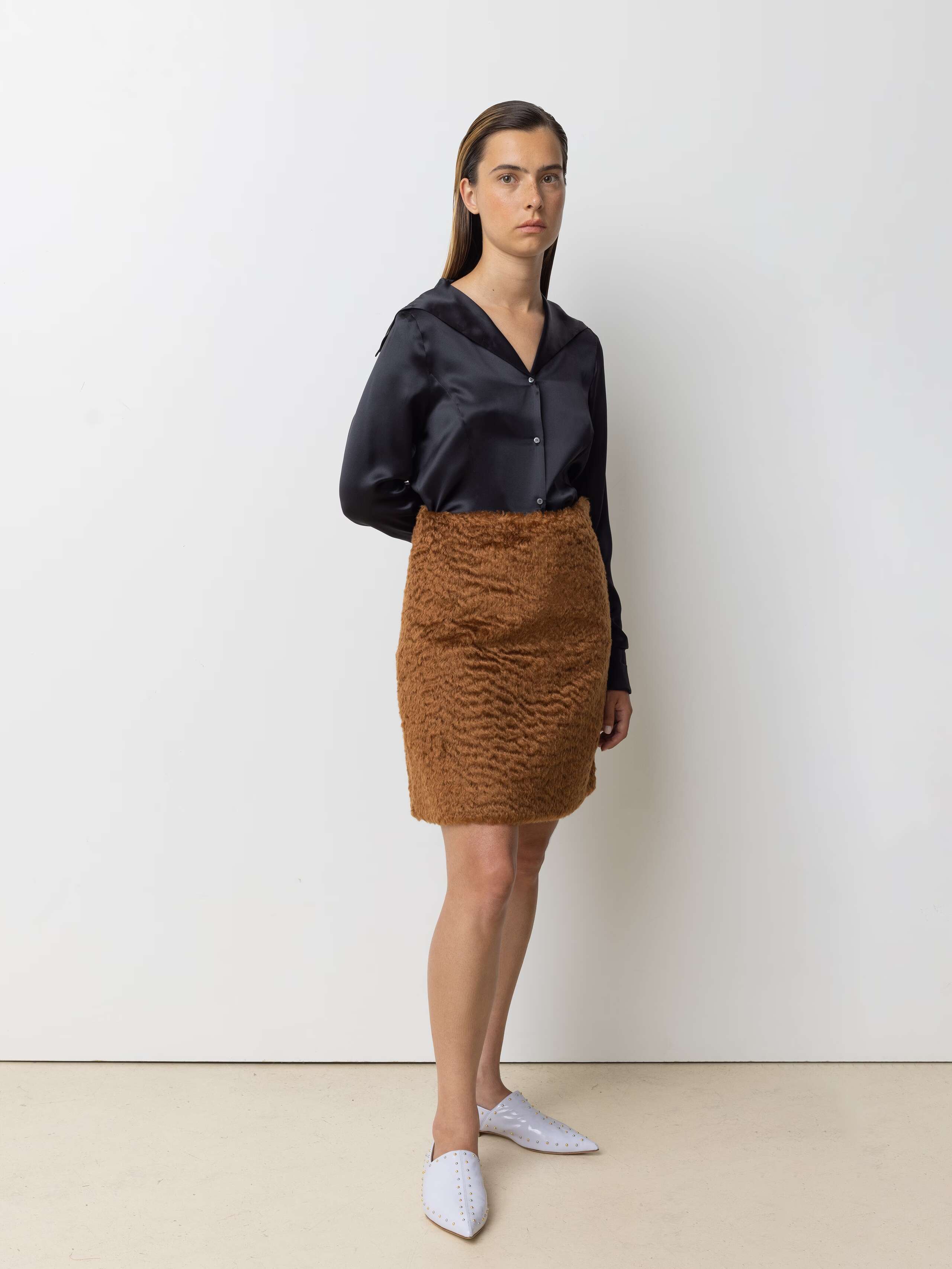 Picture of a female model wearing a short brown skirt in combination with a silk blouse in a black shade