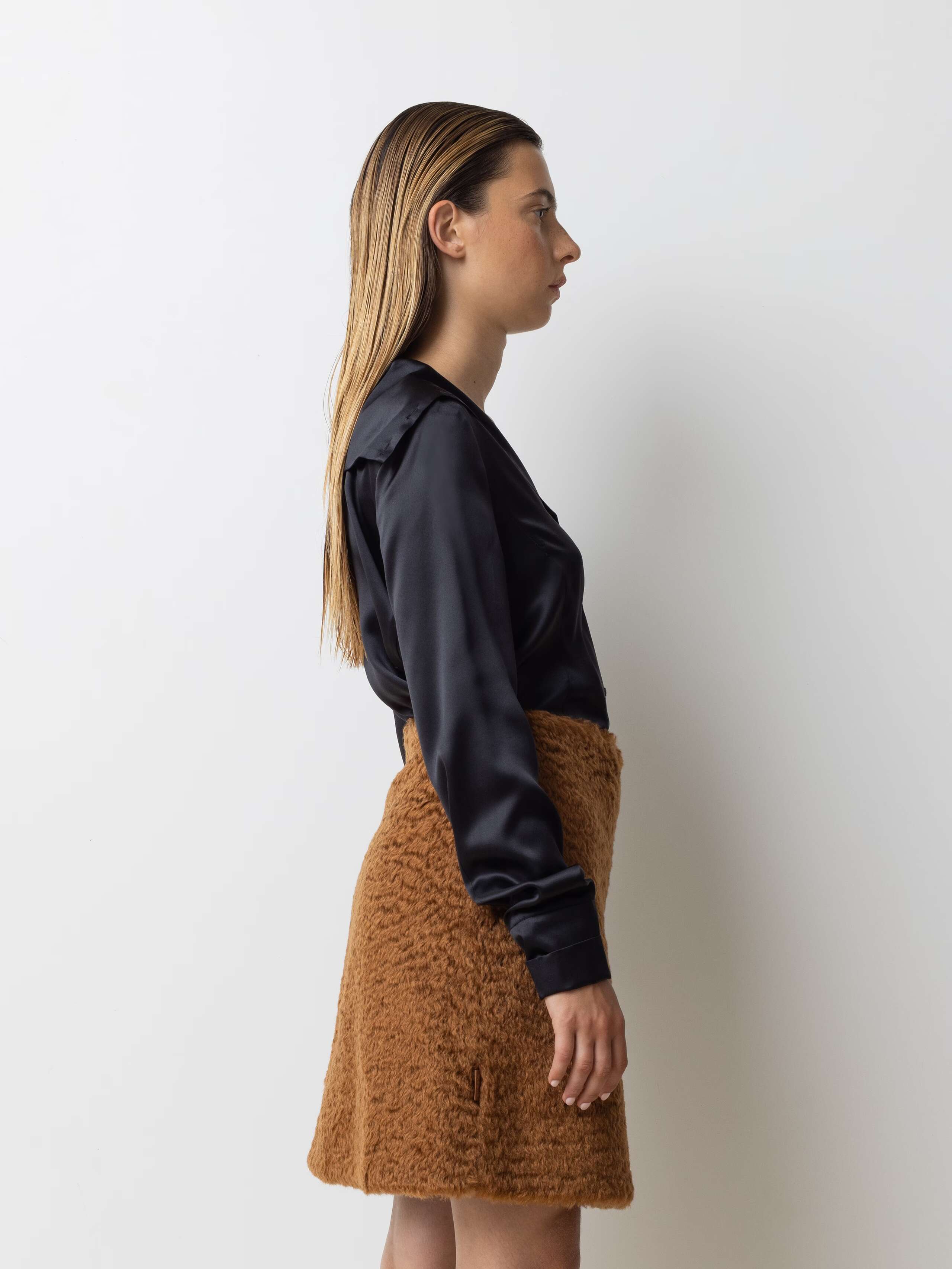 Picture of a female model wearing a short brown skirt in combination with a silk blouse in a black shade