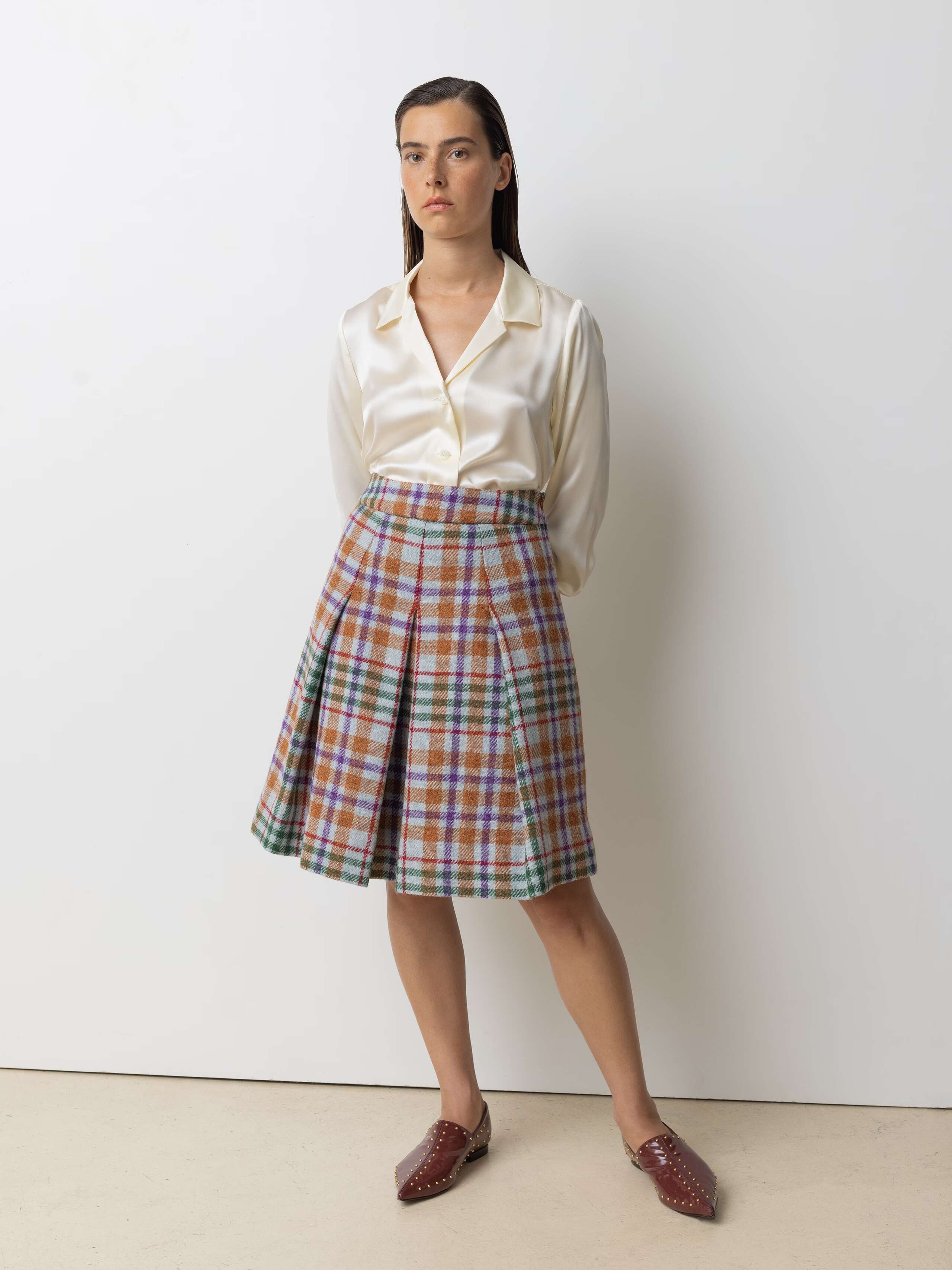 Picture of a female model wearing a medium long wool skirt in shades of bright blue, green and red shades combined with a beige silk blouse