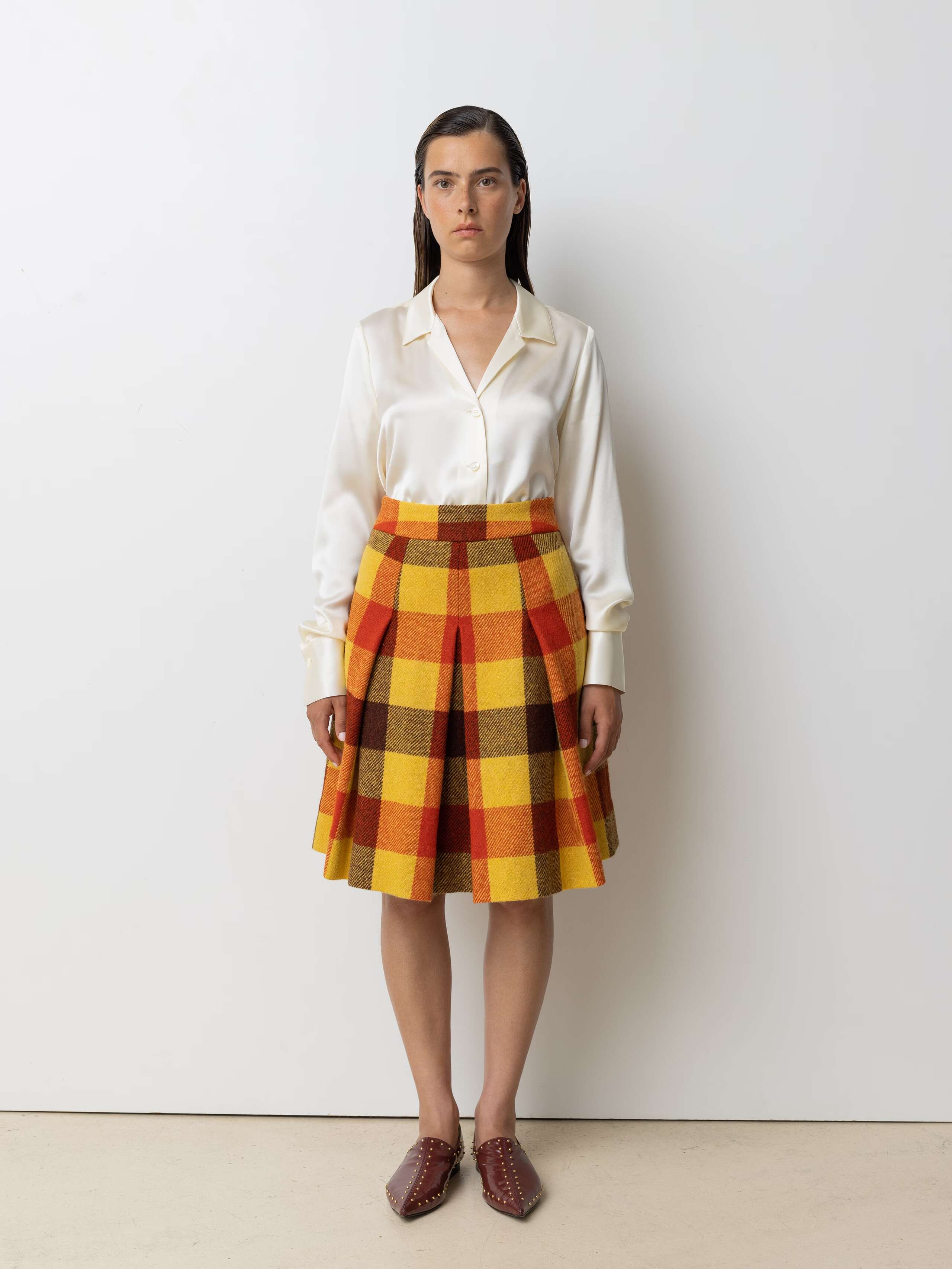 Picture of a female model wearing a medium long wool skirt in shades of bright red, yellow and brown combined with a beige silk blouse