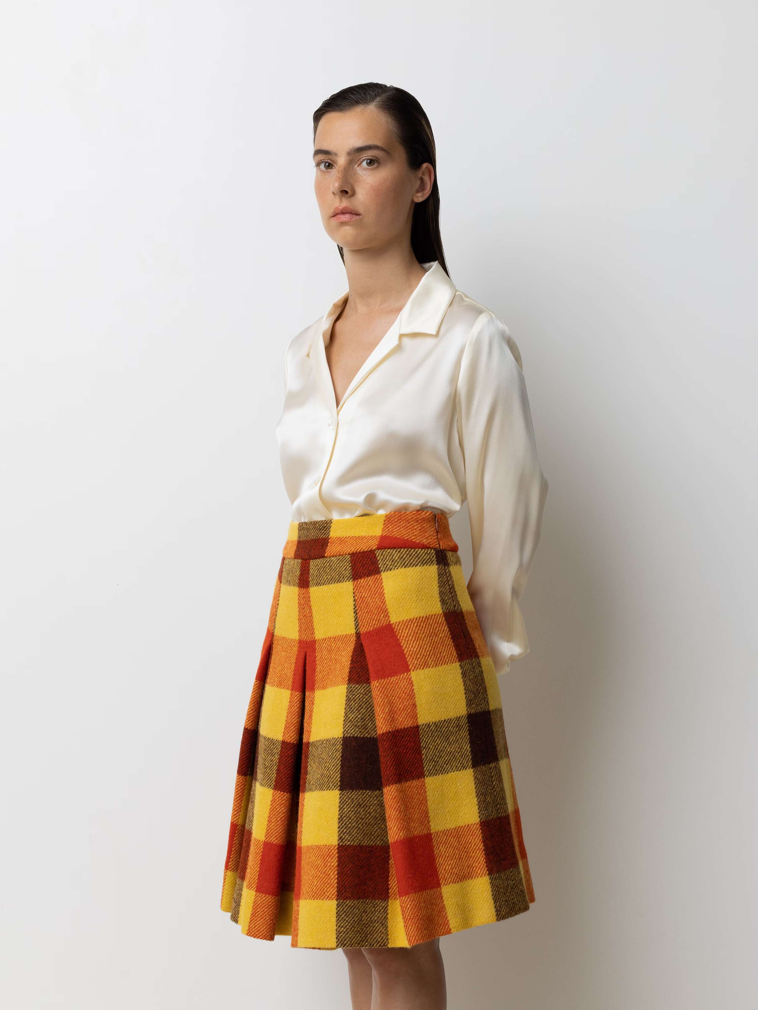 Picture of a female model wearing a medium long wool skirt in shades of bright red, yellow and brown combined with a beige silk blouse