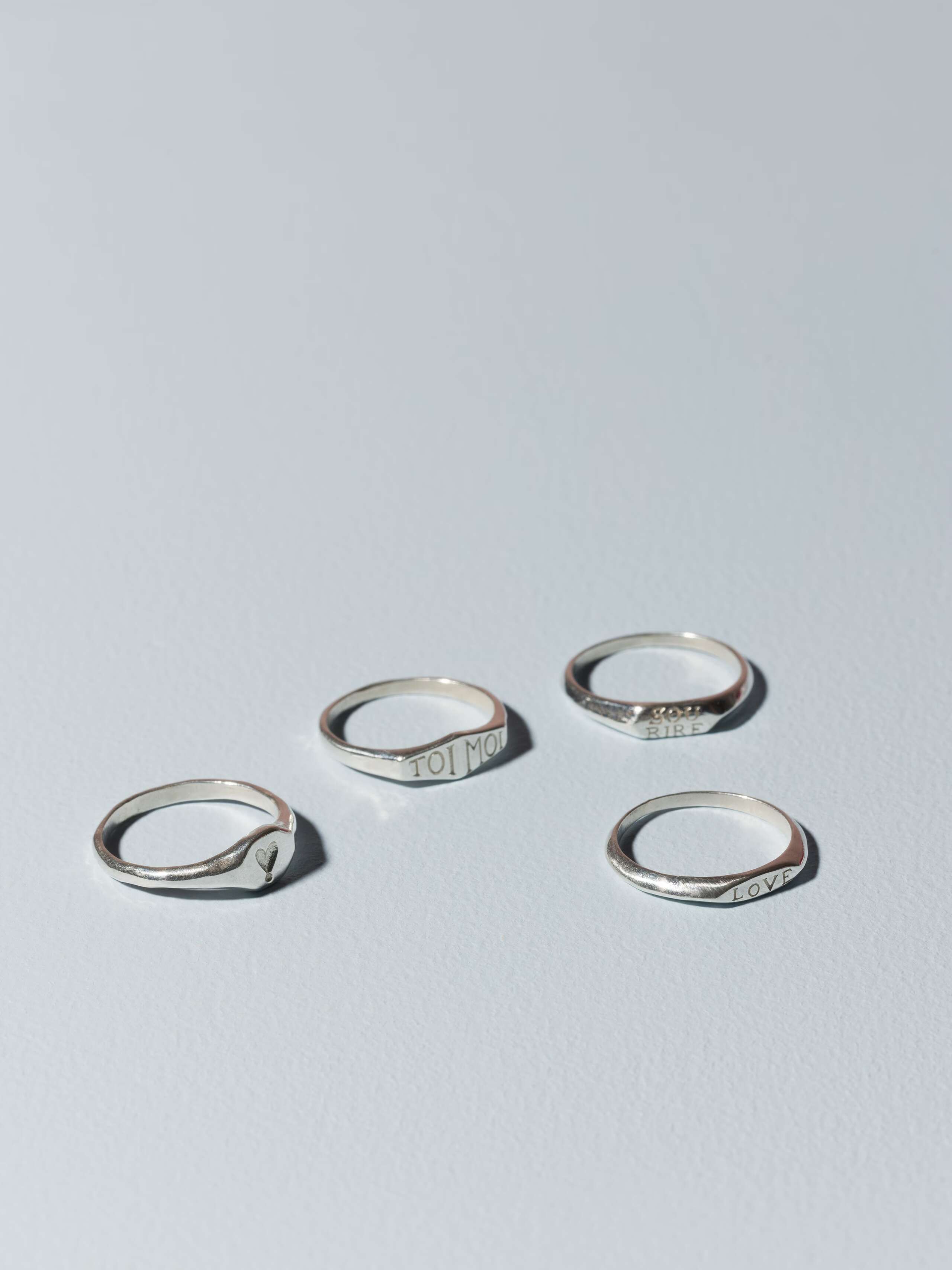 Group of small sterling silver signet rings called Ida on plain background