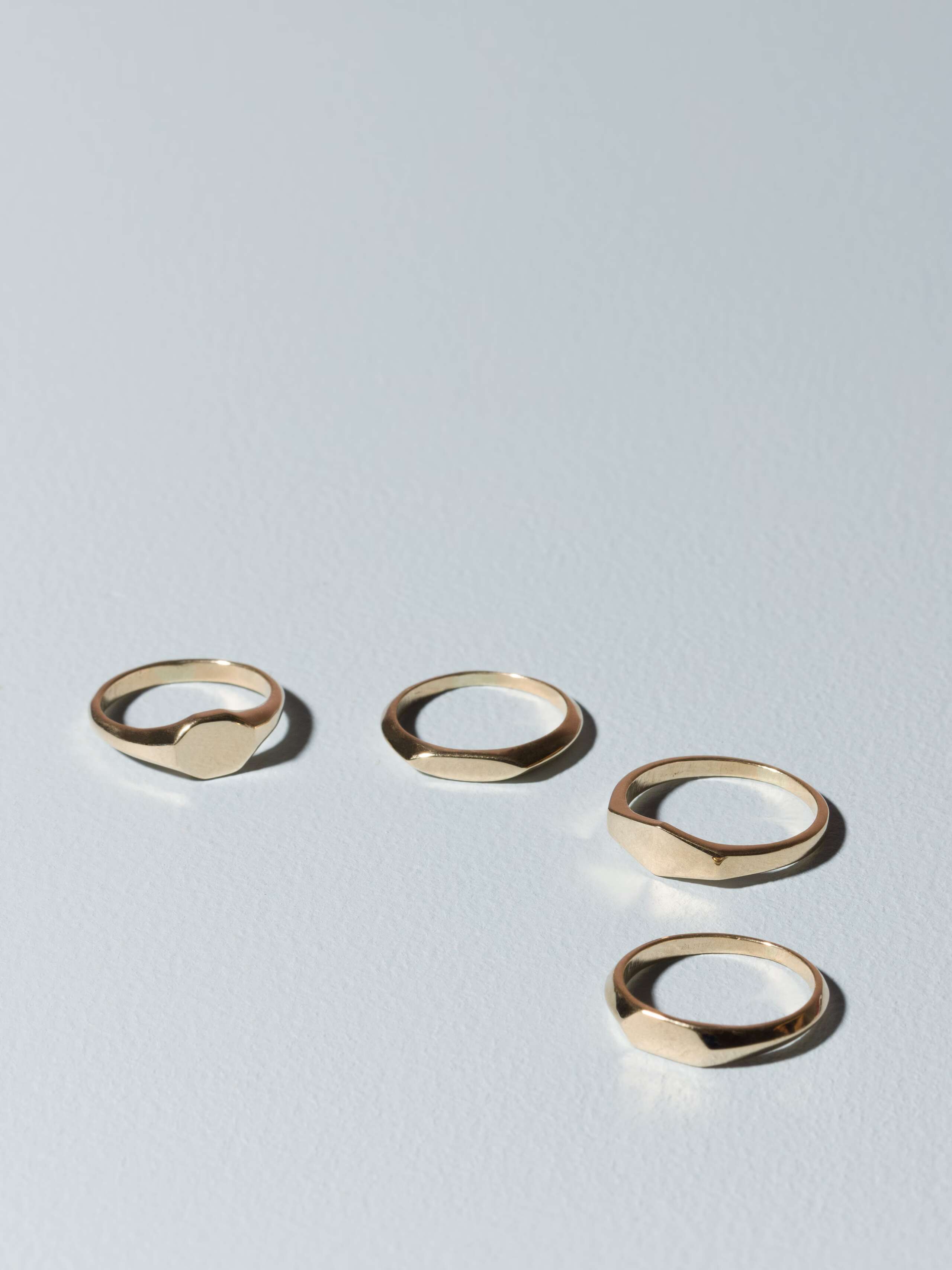 Group of small 9 karat gold signet rings called Ida on plain background