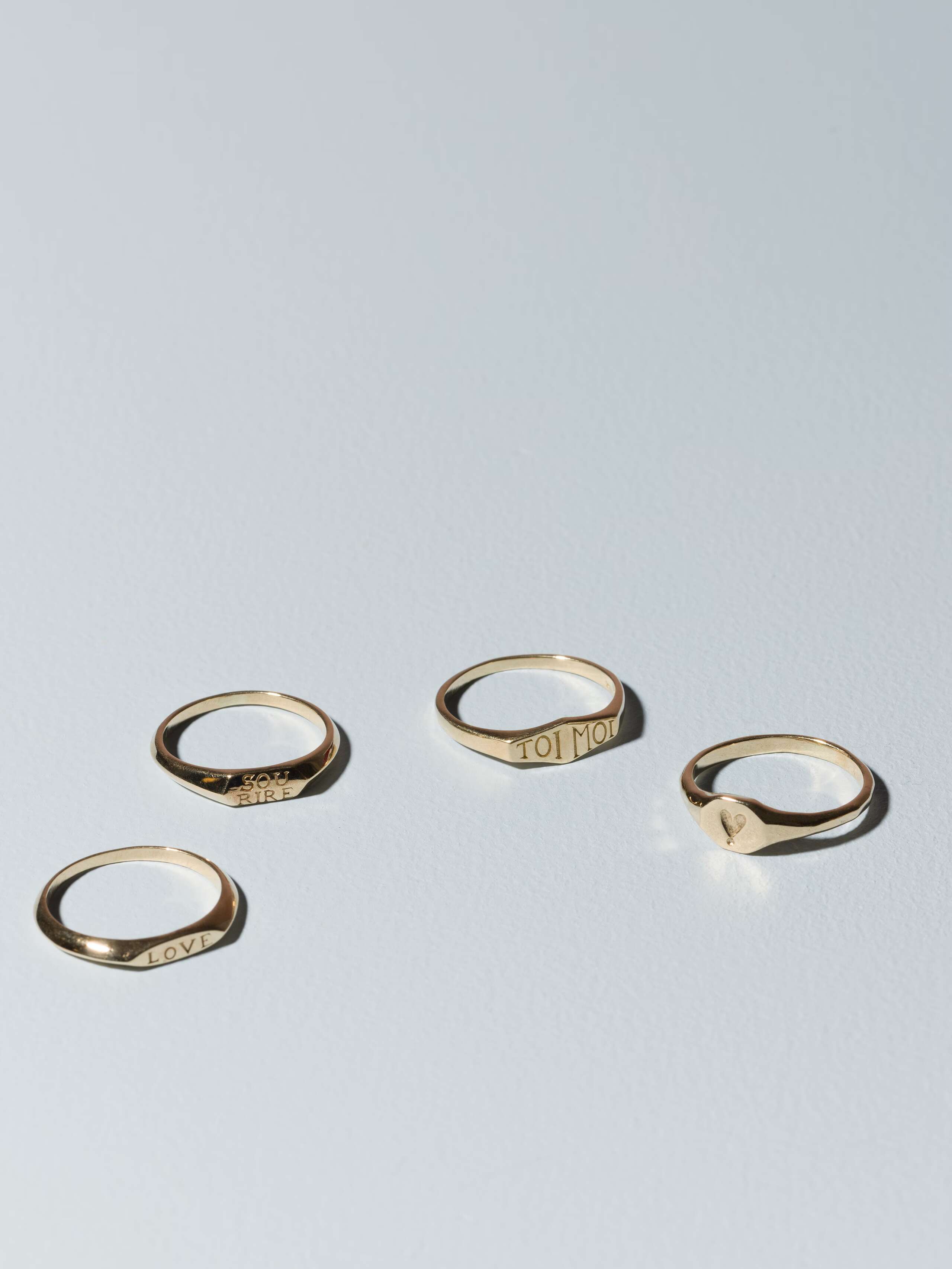Group of small 9 karat gold signet rings called Ida on plain background