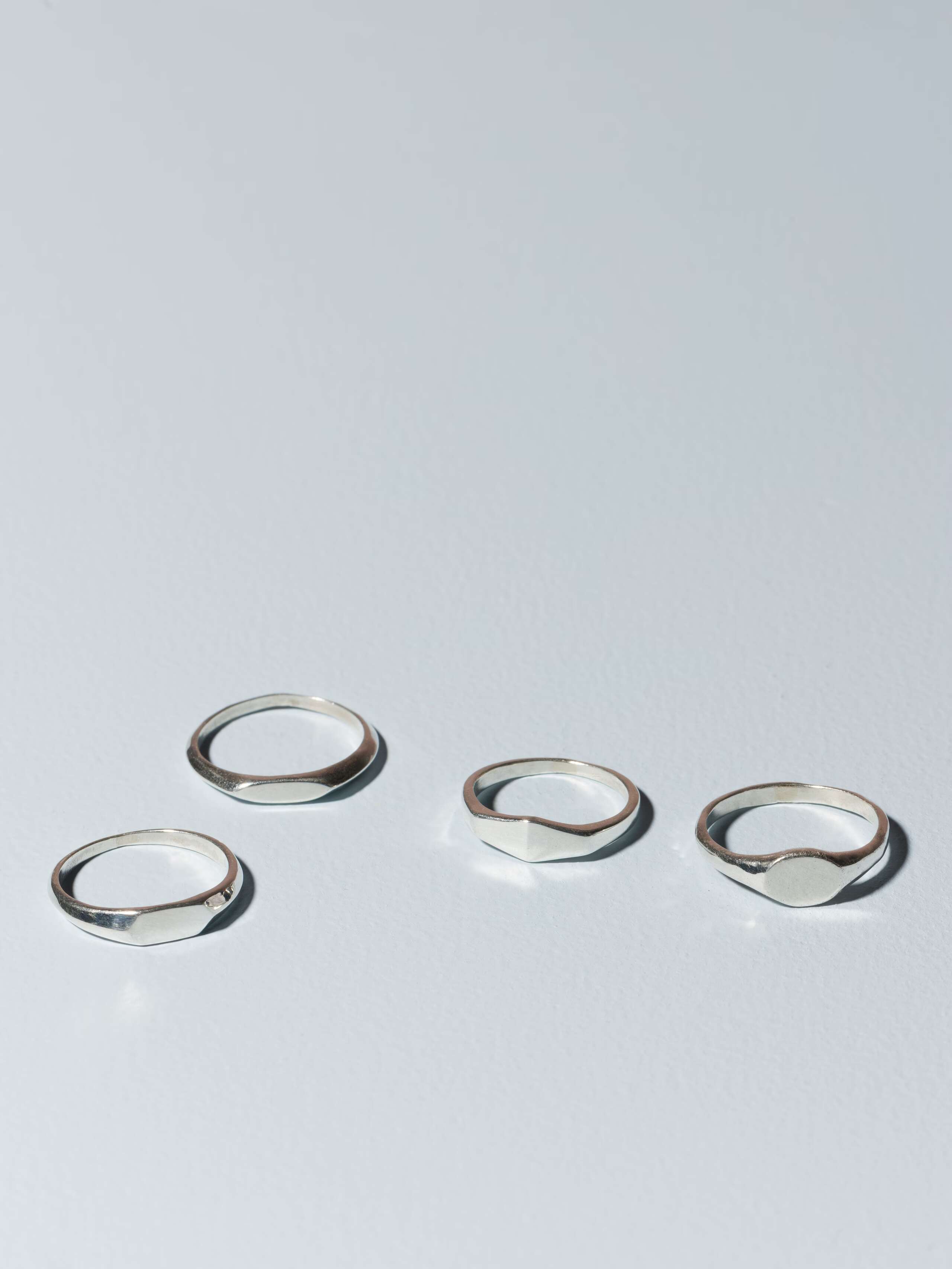 Group of small sterling silver signet rings called Ida on plain background