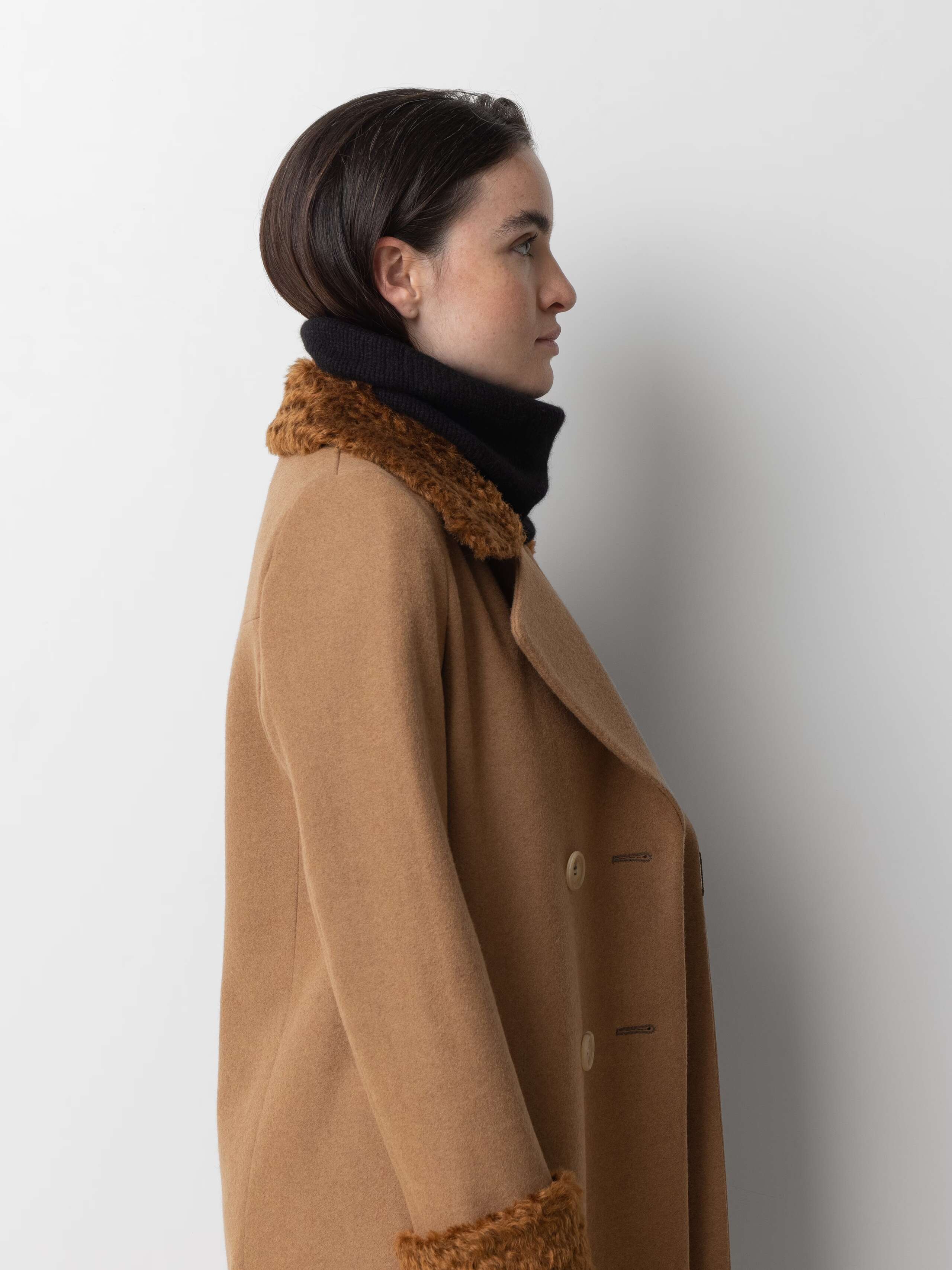 Picture of a female model wearing a beige wool coat in combination with a black tube hat