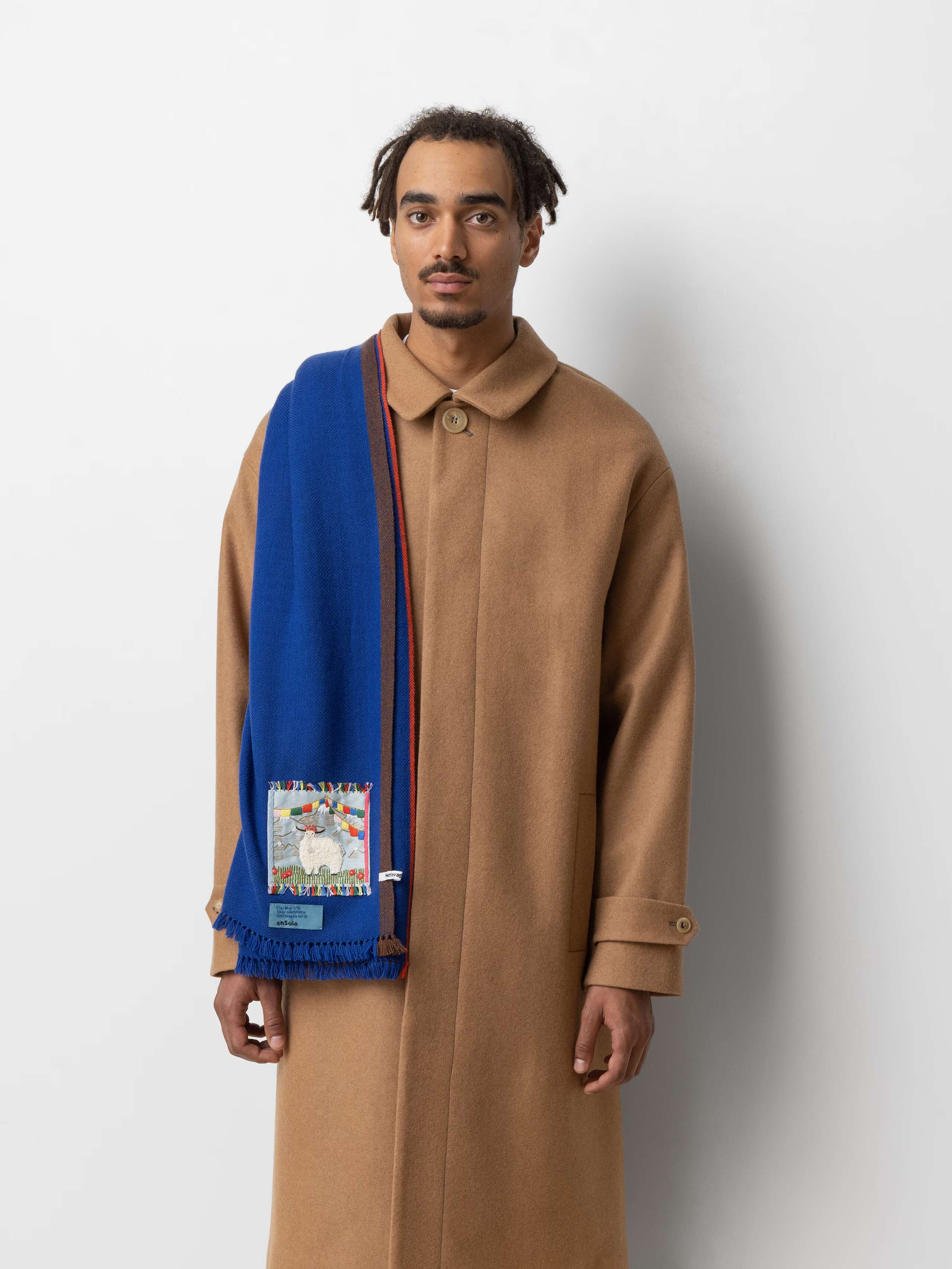 Picture of a male model wearing a beige winter coat and a blue cashmere stole