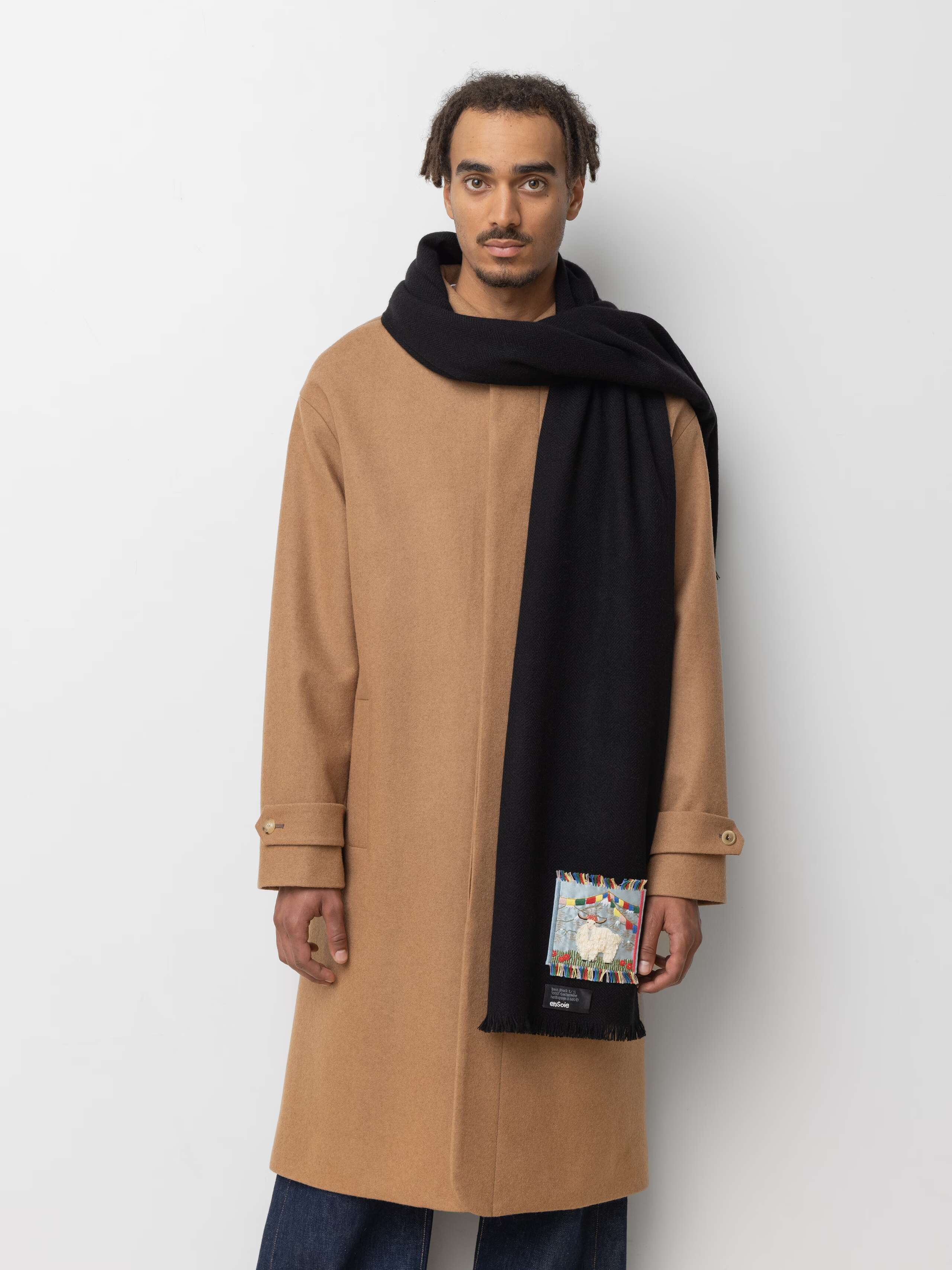 Picture of a male model wearing a beige wool coat and a black cashmere scarf