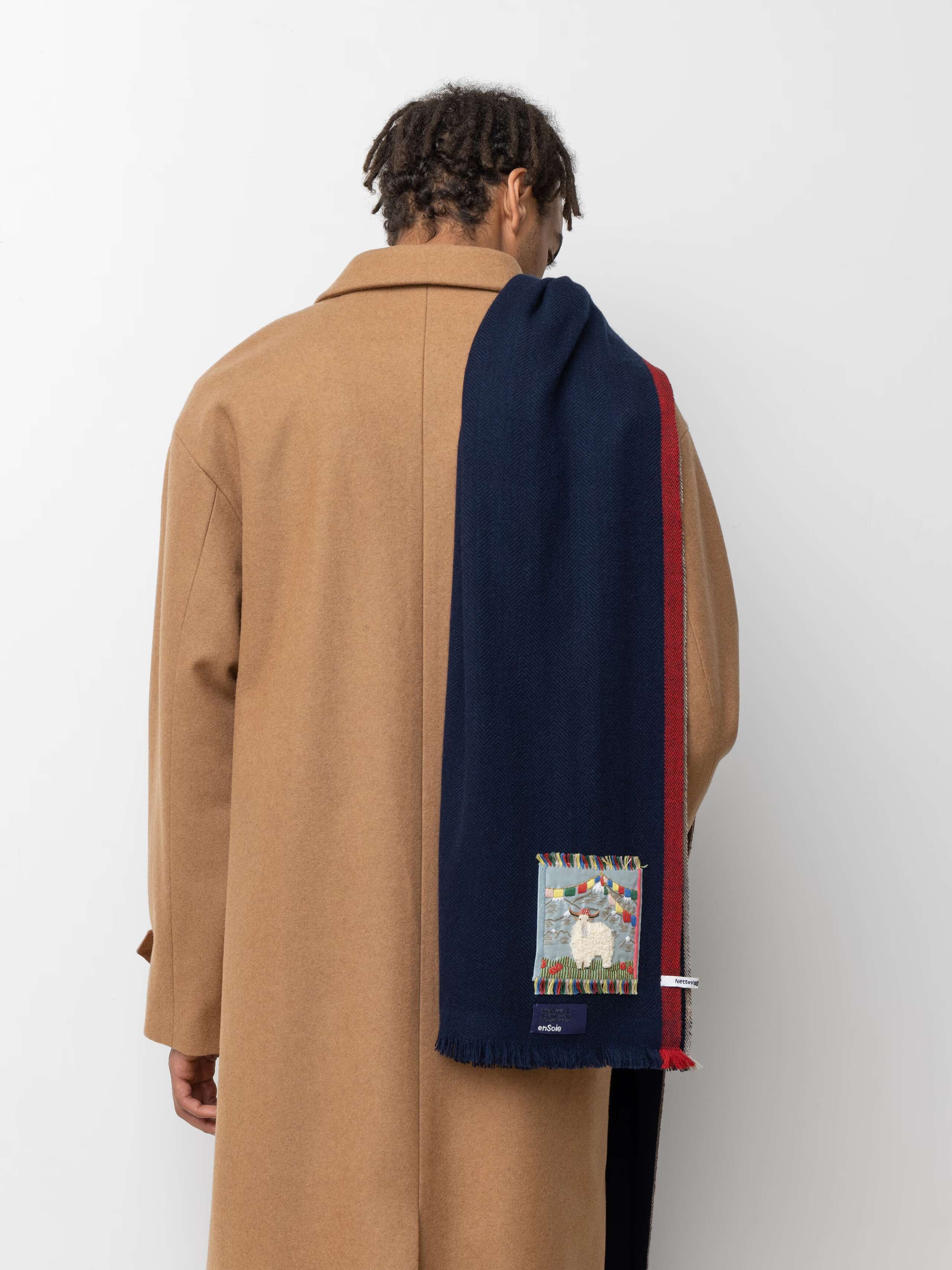 Picture of a male model wearing a beige wool coat and a navy blue cashmere scarf