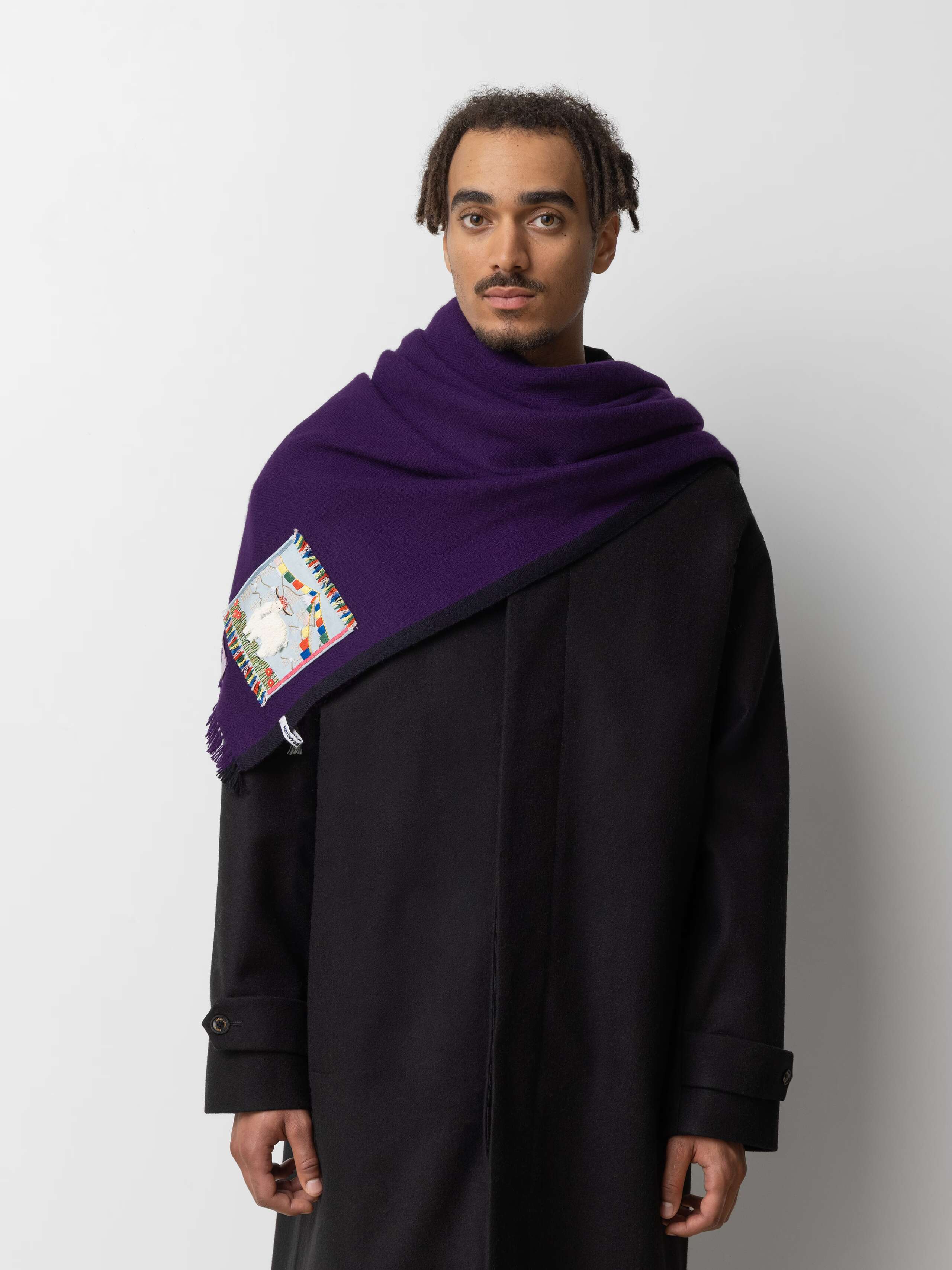 Picture of a male model wearing a black wool coat in combination with a deep purple cashmere stole