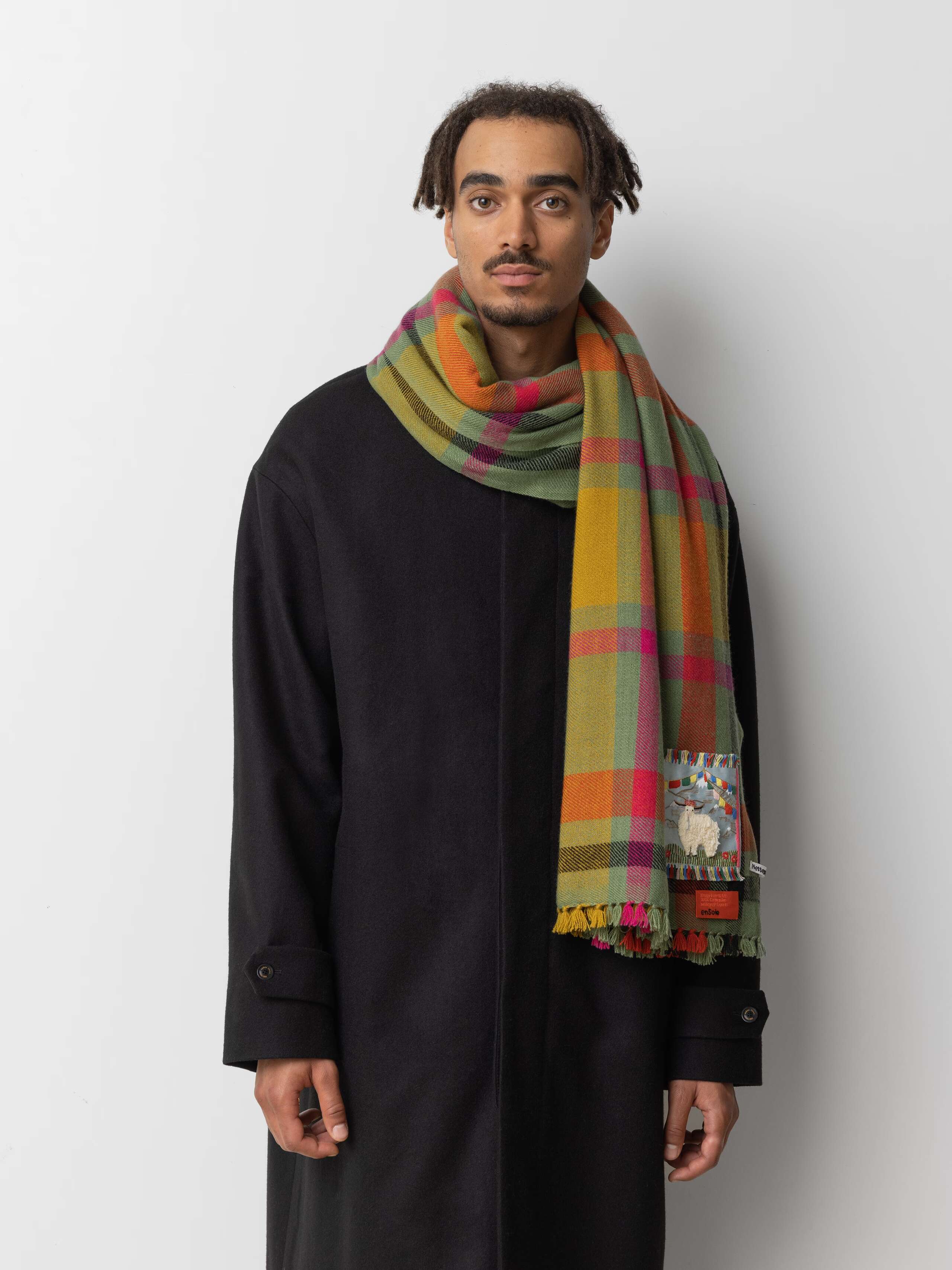 Picture of a male model wearing a black wool coat in combination with a colourful cashmere stole