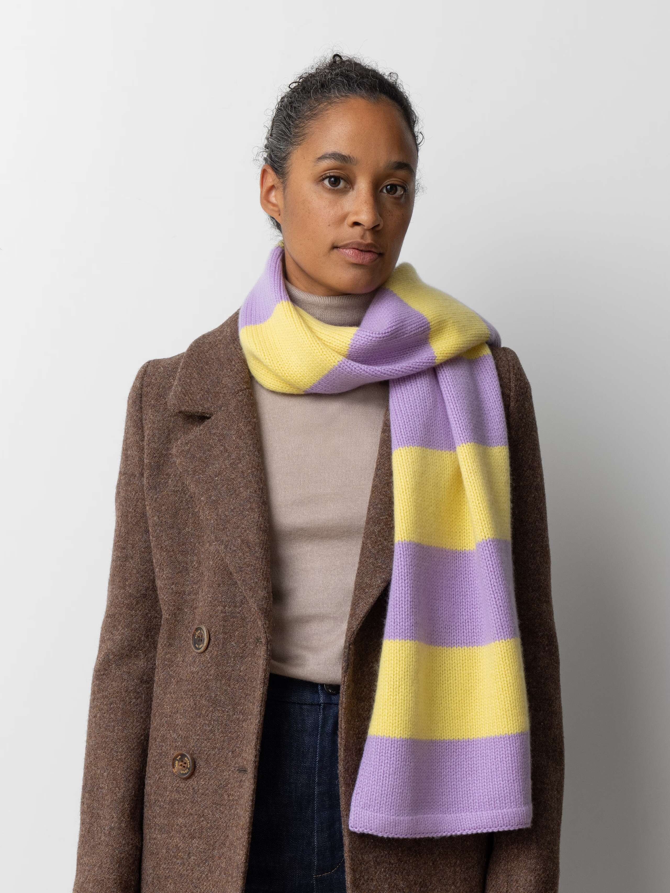 Picture of a female model wearing a brown wool jacket and a yellow and purple striped cashmere scarf