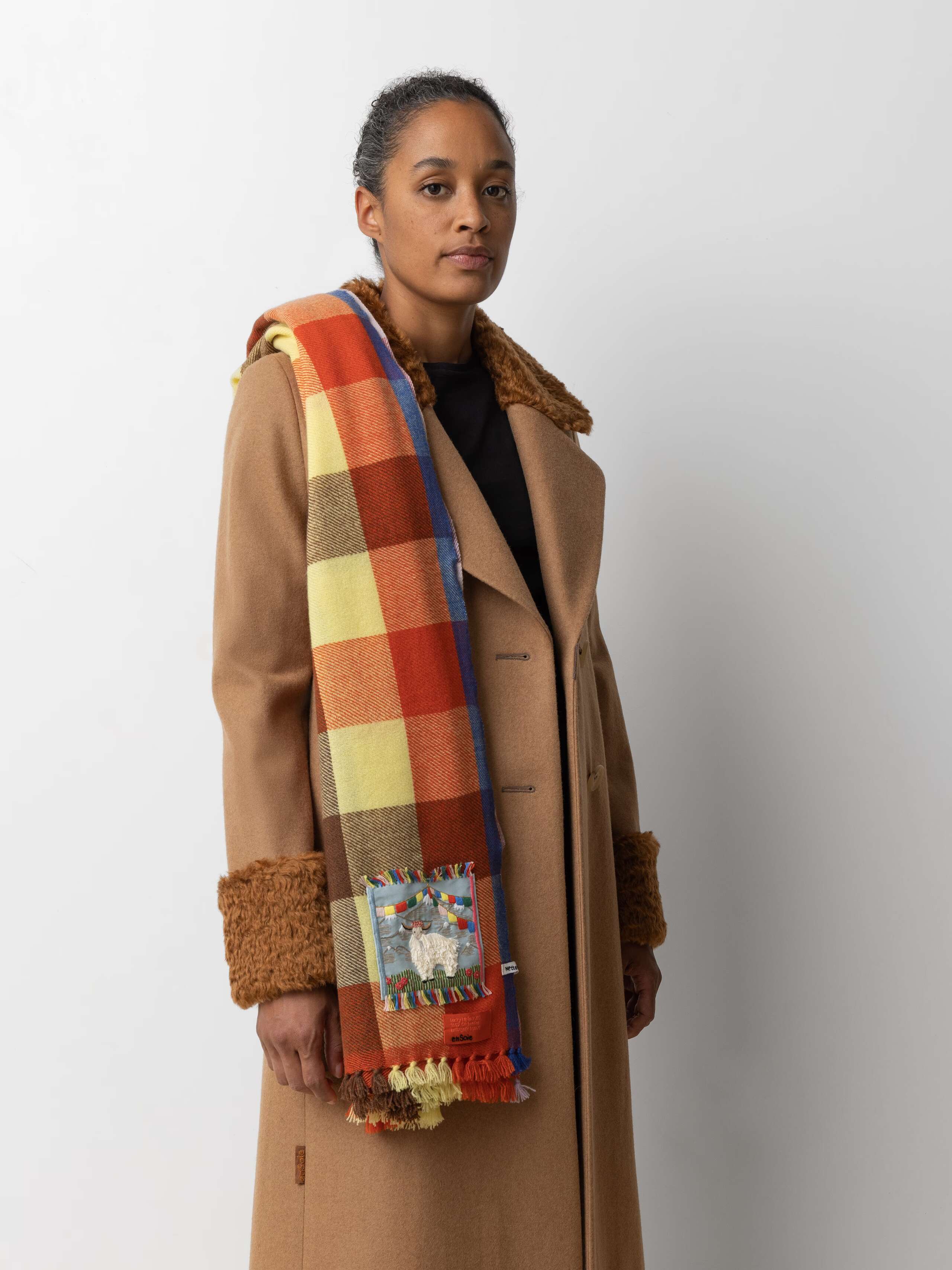 Picture of a female model wearing a beige wool coat in combination with a colourful cashmere stole