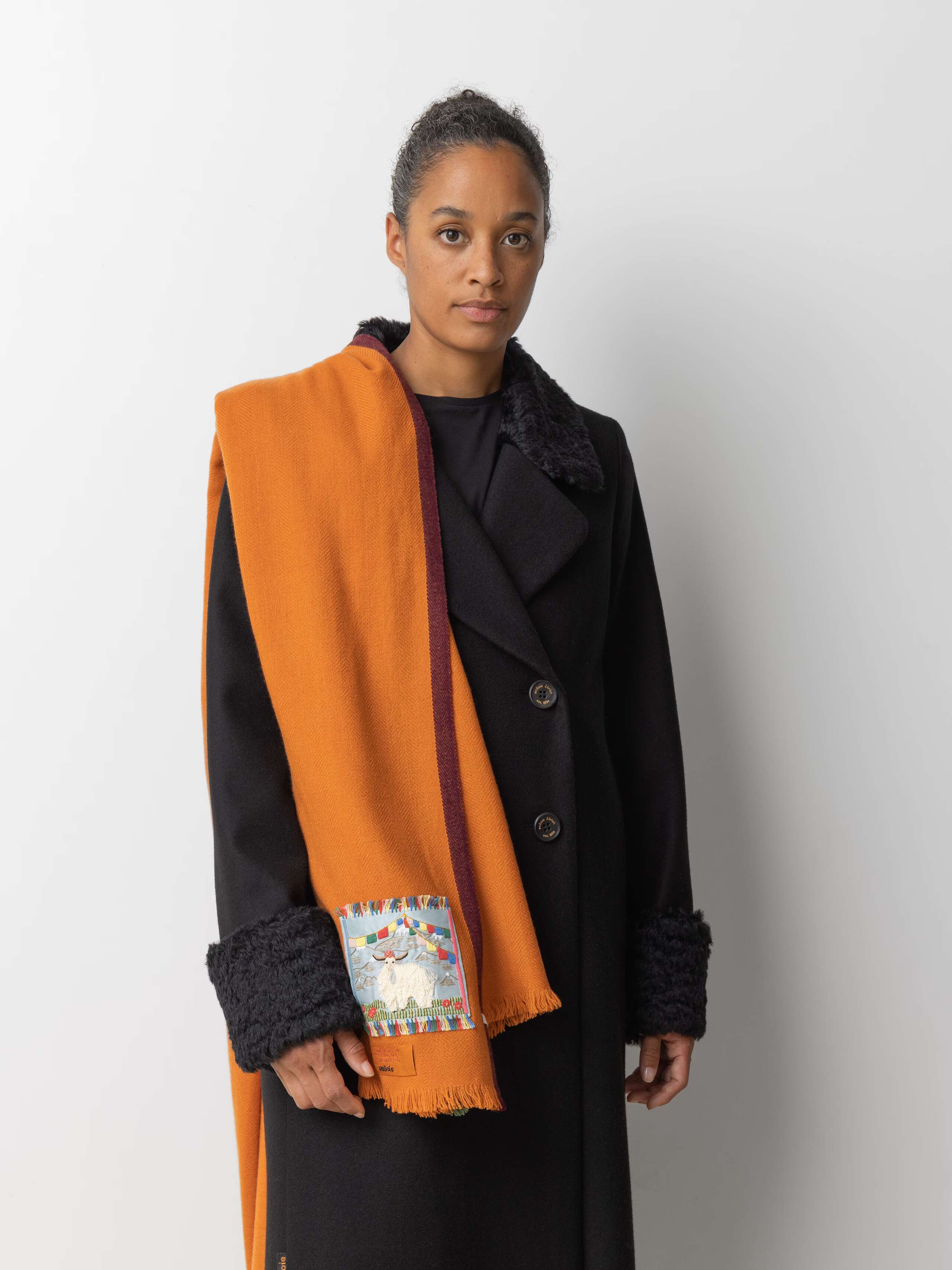Picture of a female model wearing a black wool coat and a orange cashmere stole