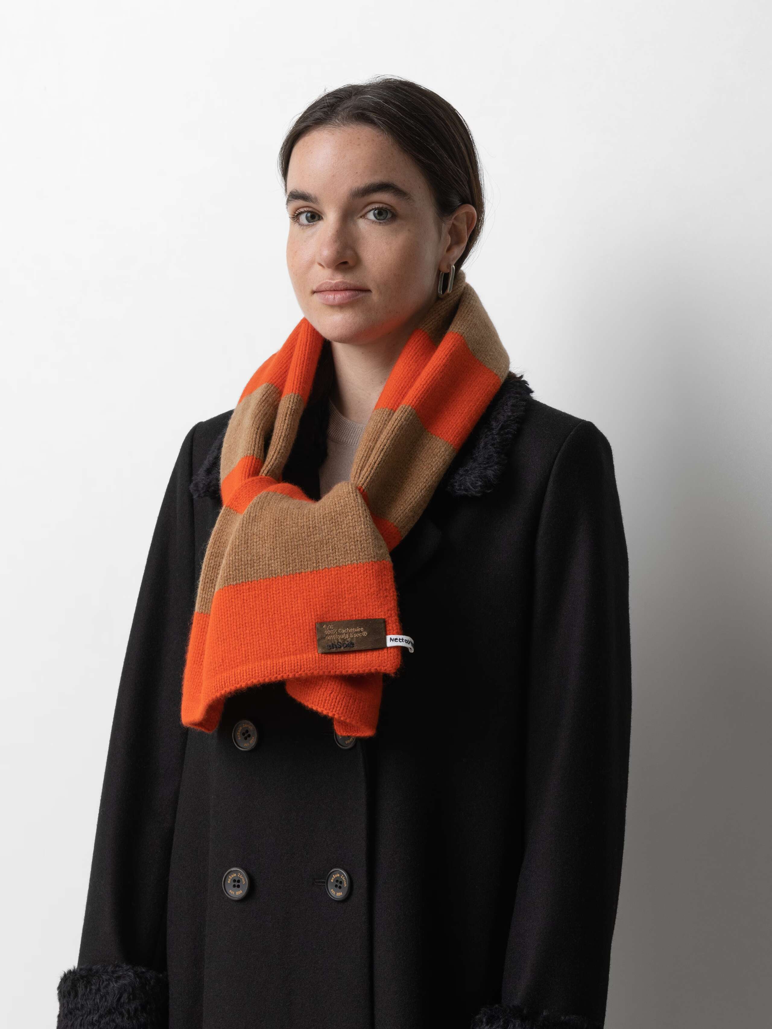 Picture of a female model wearing a black winter coat in combination with a brown and orange striped cashmere scarf