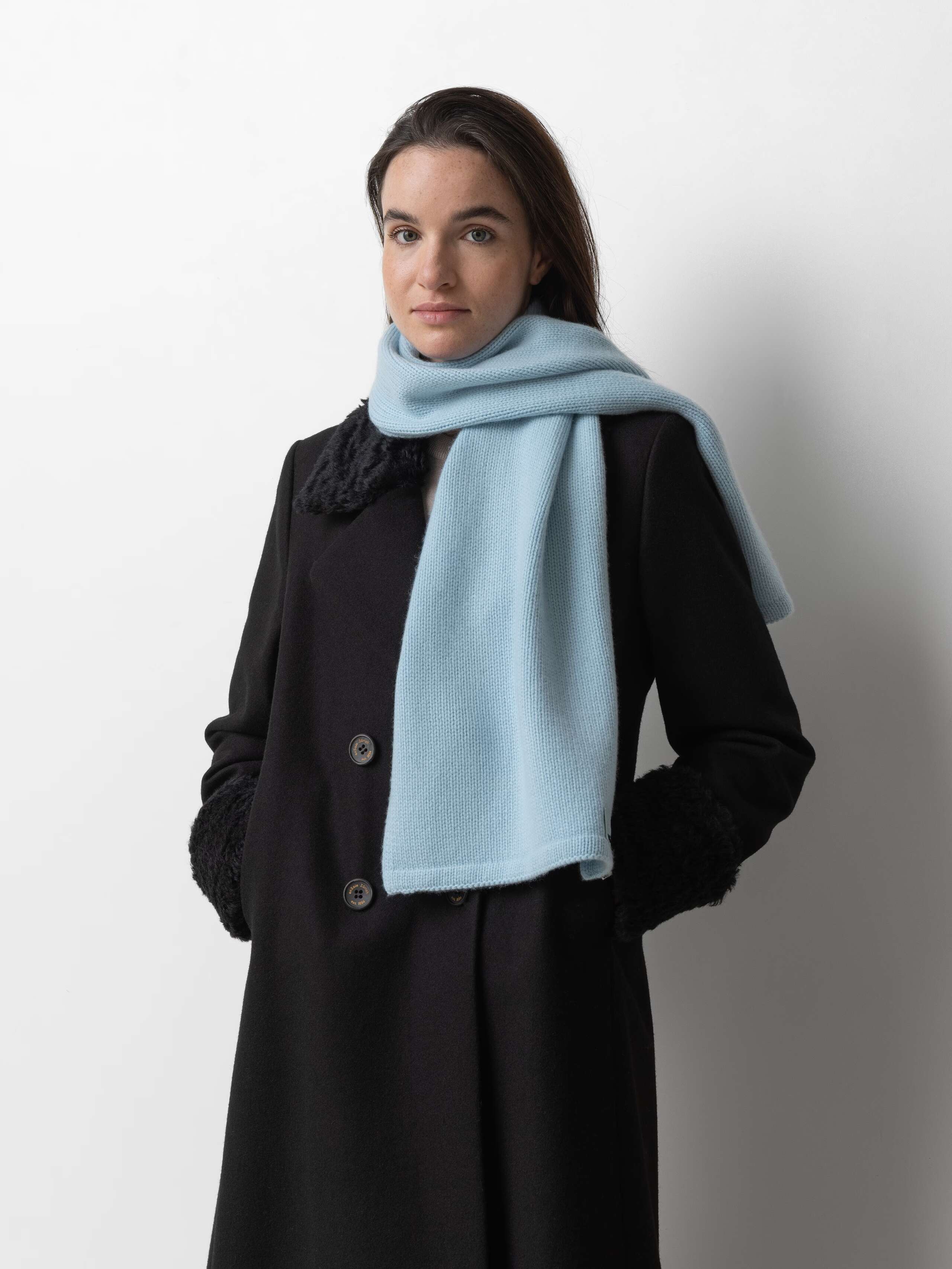 Picture of a female model wearing a black winter coat in combination with a light blue cashmere scarf