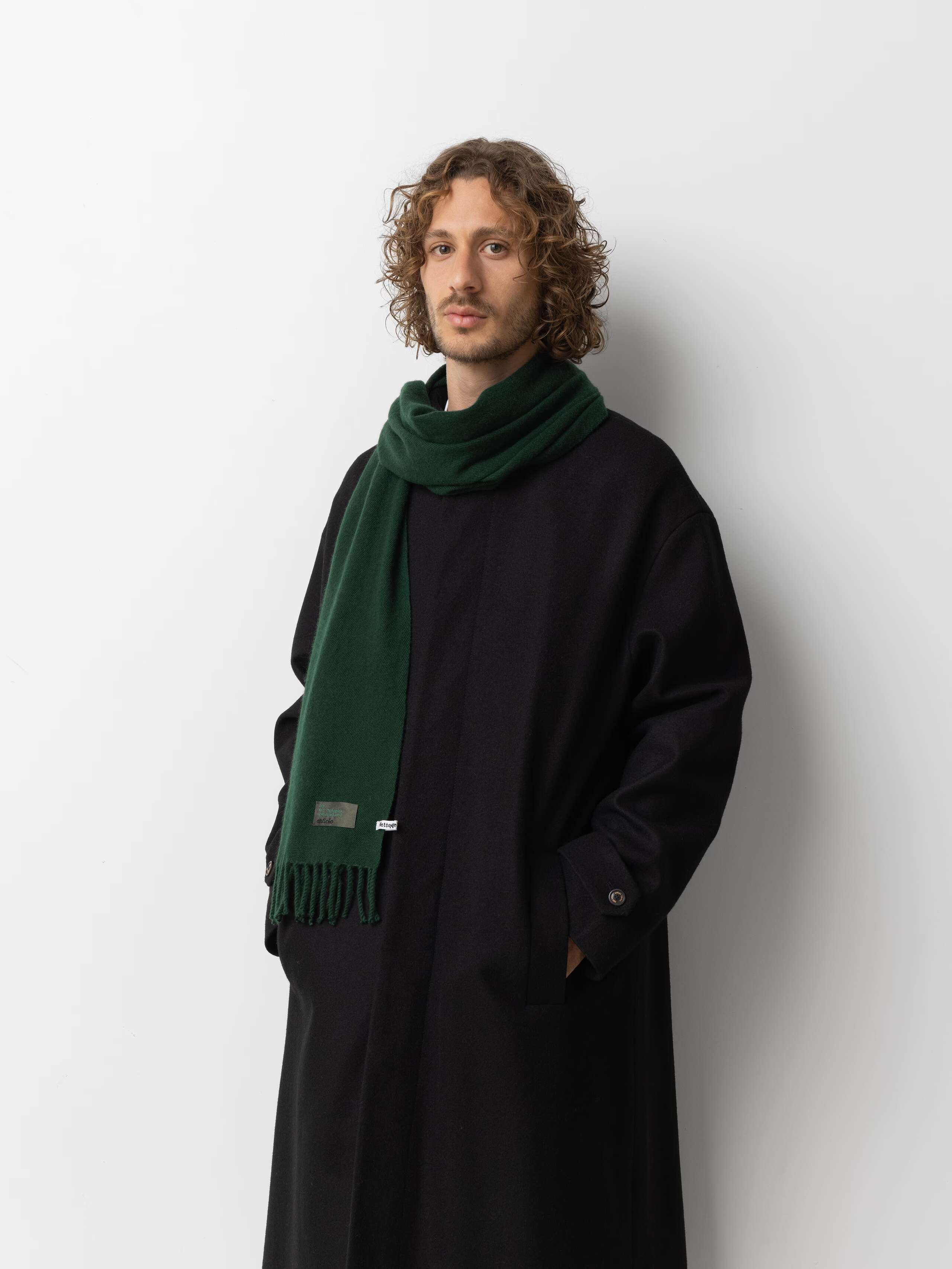 Picture of a male model wearing a black wool coat in combination with a green cashmere scarf