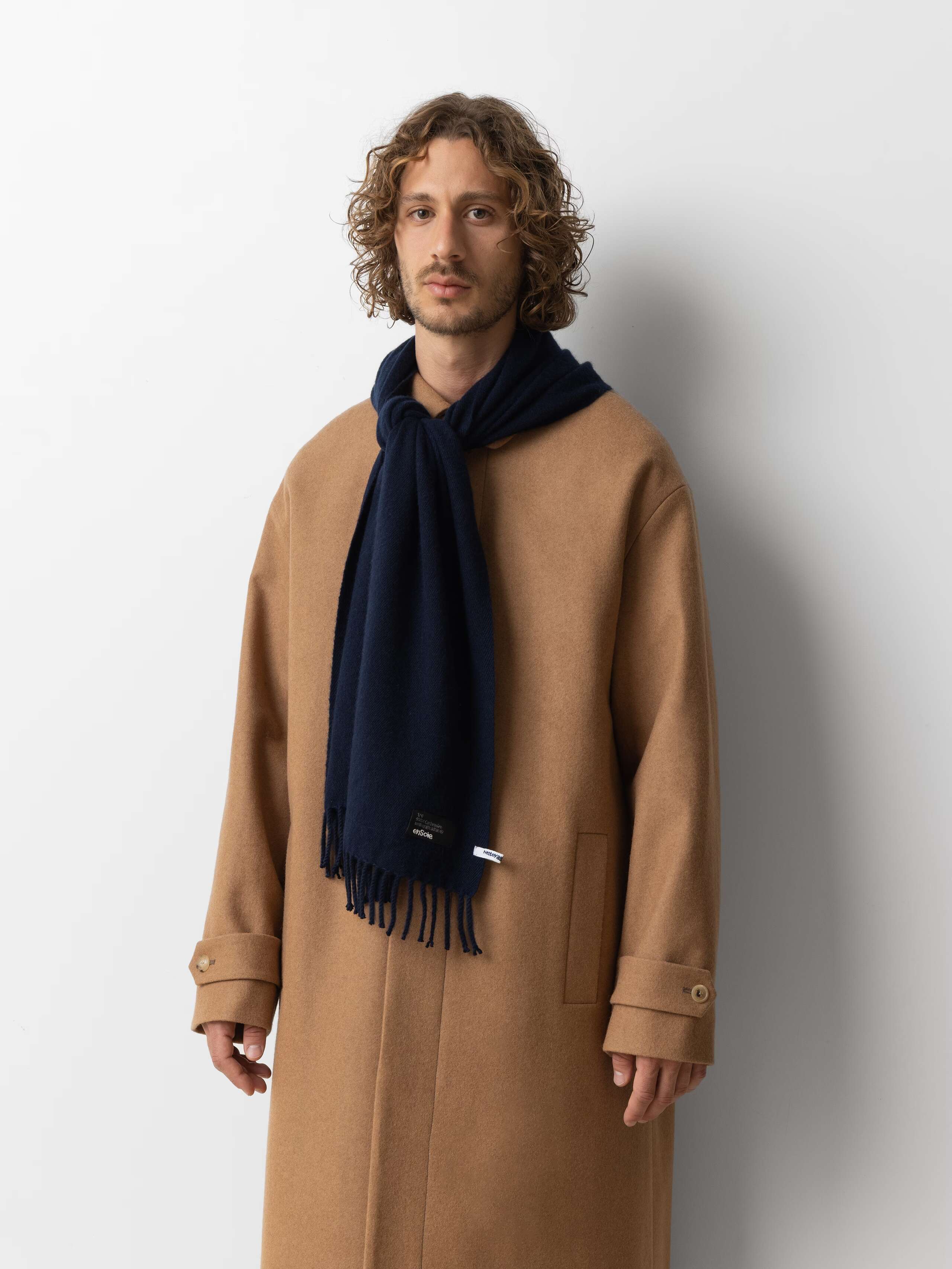 Picture of a male model wearing a beige wool coat in combination with a black cashmere scarf