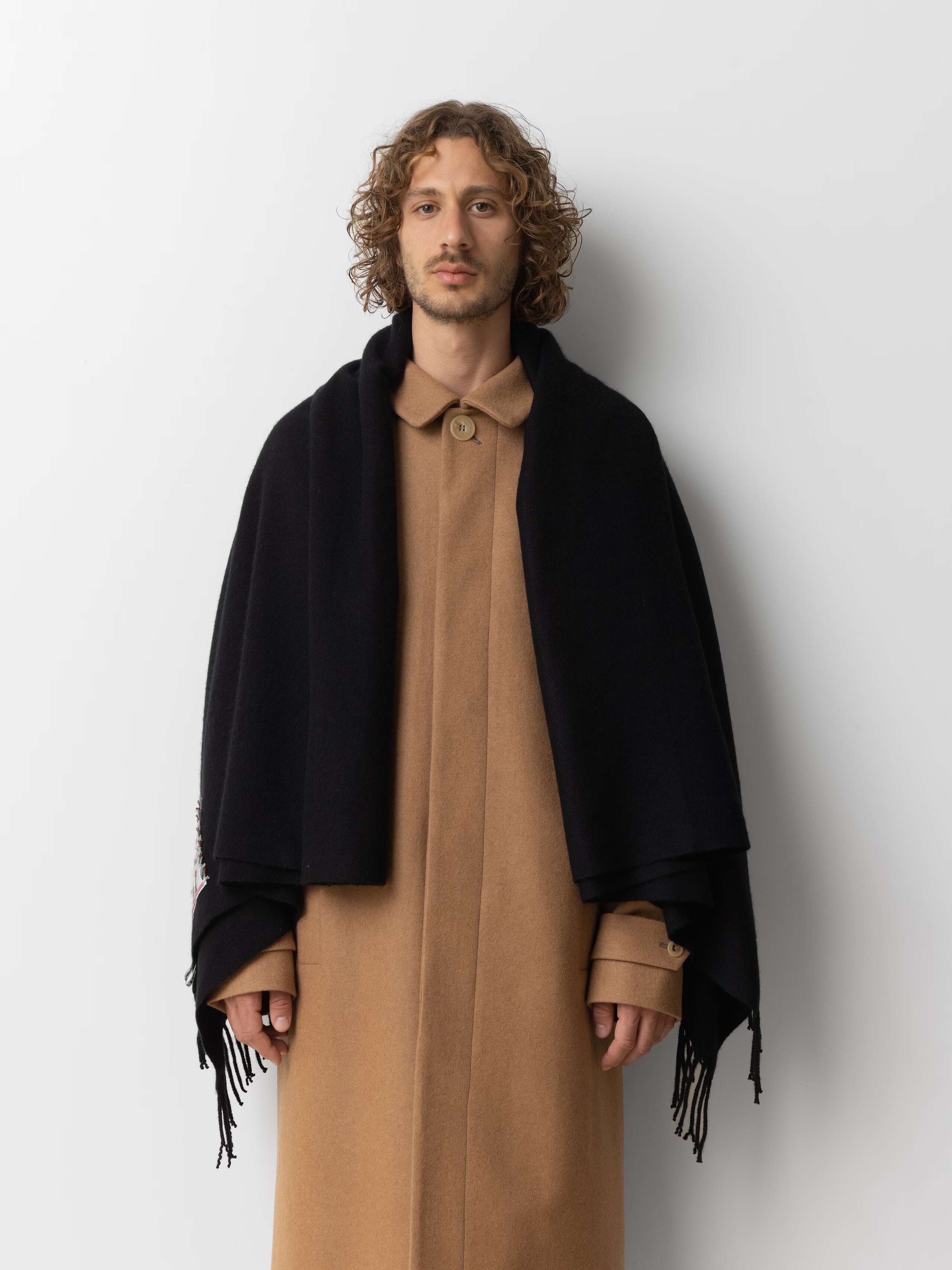 Picture of a male model wearing a beige wool coat in combination with a black cashmere stole